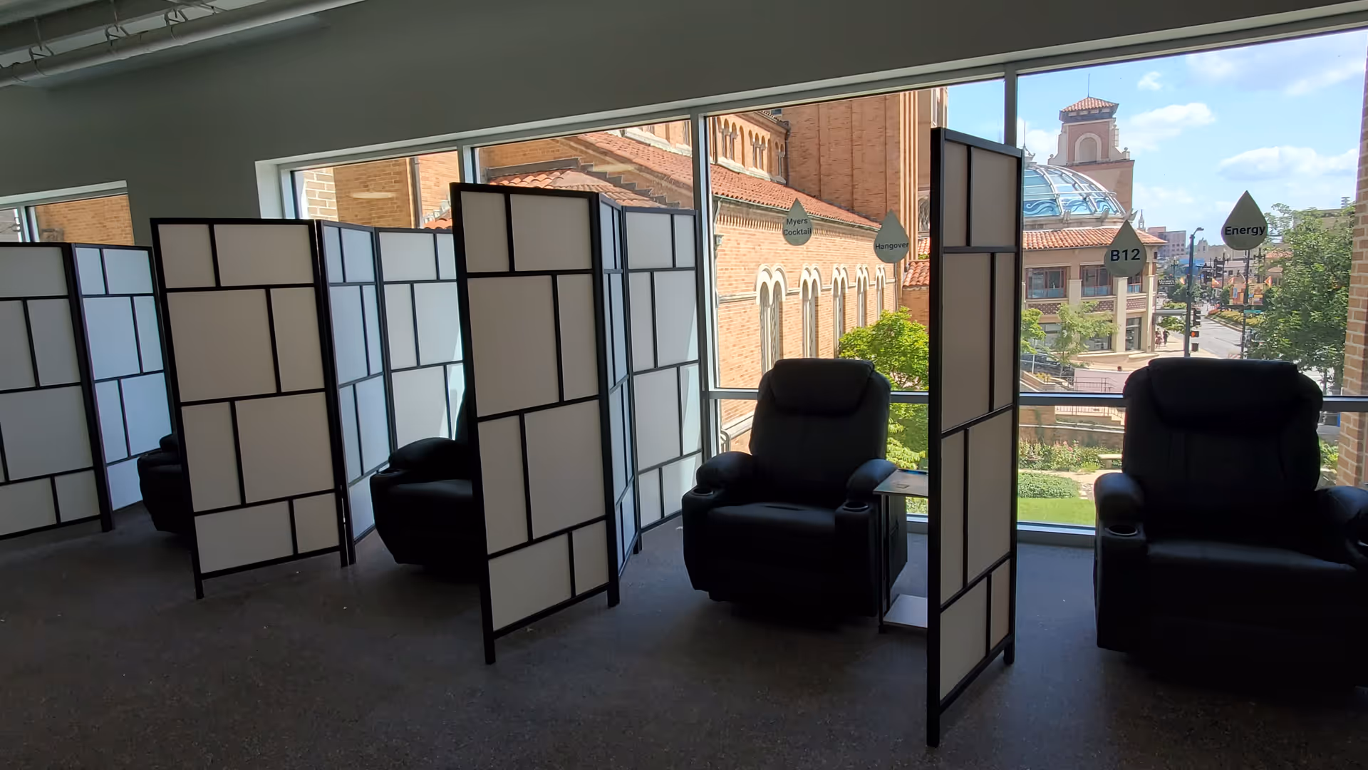 Interior lounge with privacy screens and black recliner chairs by large windows.