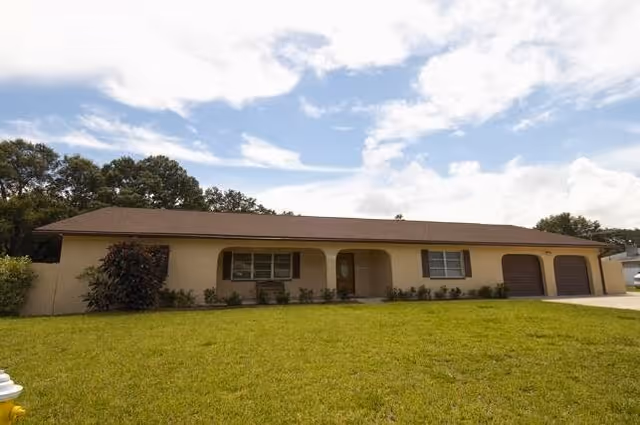 Front exterior of Communicare, Inc., a single-story beige senior living facility with arched porch.