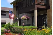 Exterior view of a senior living facility with balcony, American flag, and colorful flower beds.