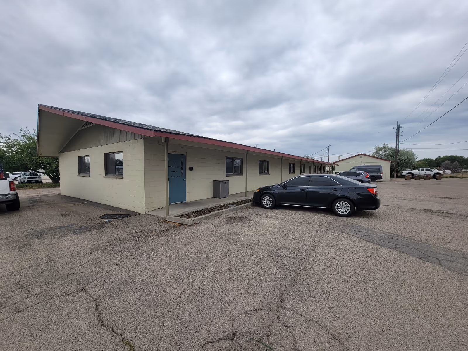 Single-story beige building with blue door and parked cars in a large lot.