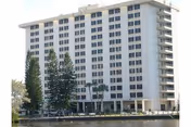 Tall white multi-story senior living building beside water with trees.