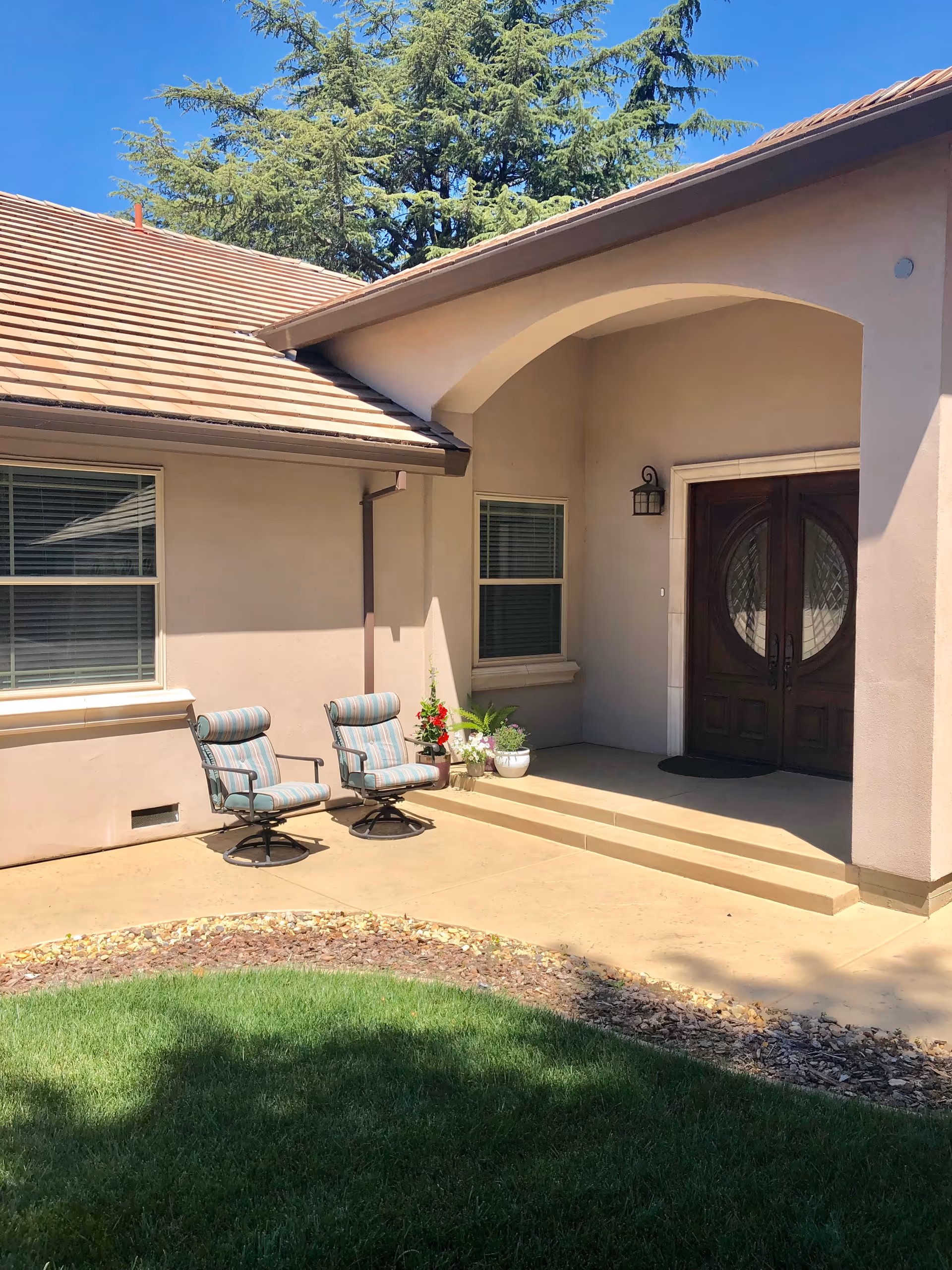 Front entrance of Silver Lining Care Home with beige stucco, arched porch, and patio chairs.