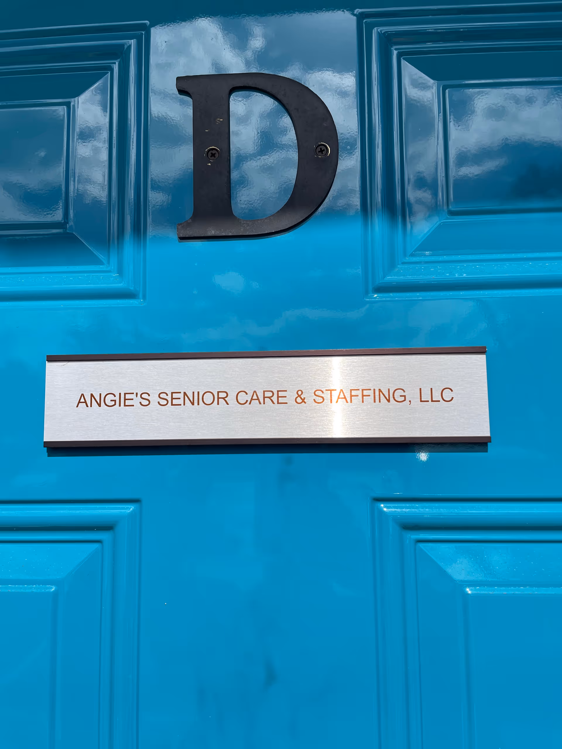 Close-up of a bright blue door with a metal plaque reading Angie’s Senior Care & Staffing.