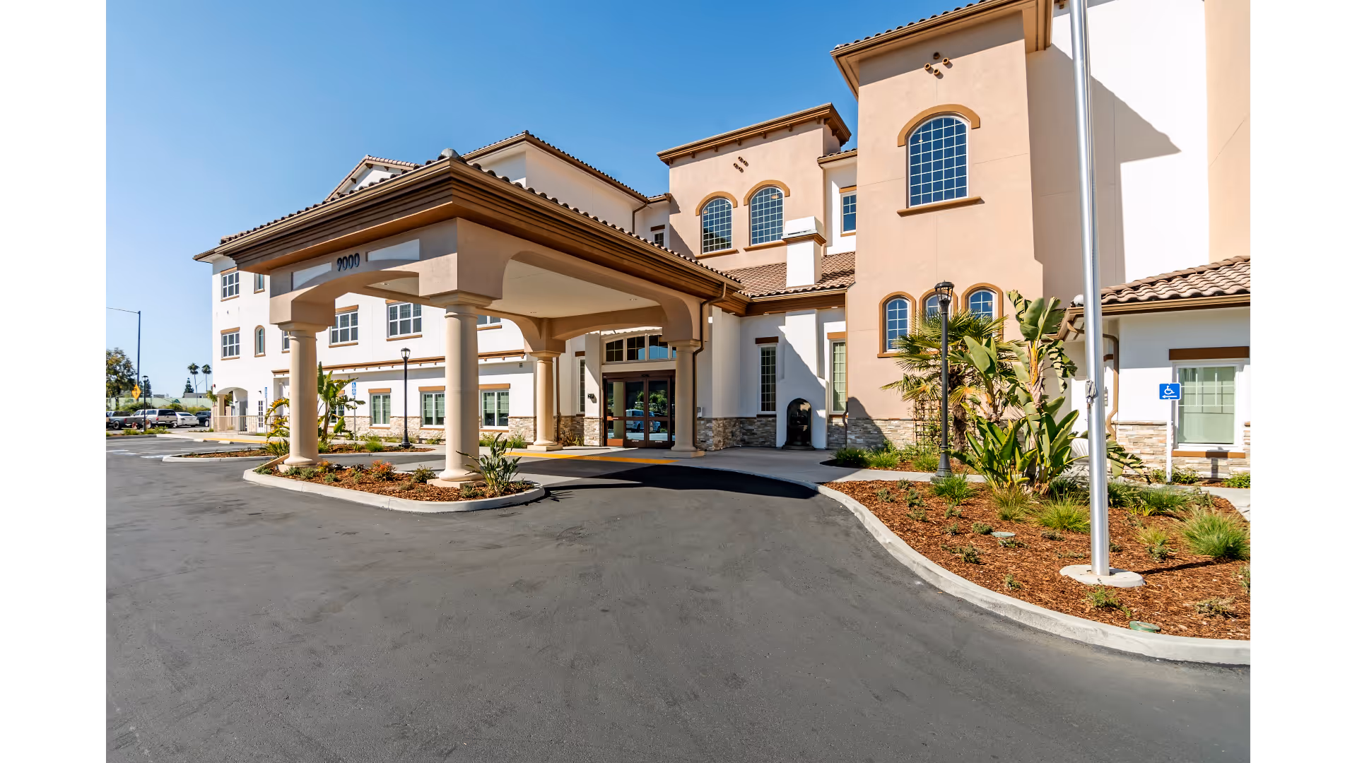 Covered entrance (porte-cochère) and front facade of a Mediterranean-style senior living building with a driveway and landscaping.