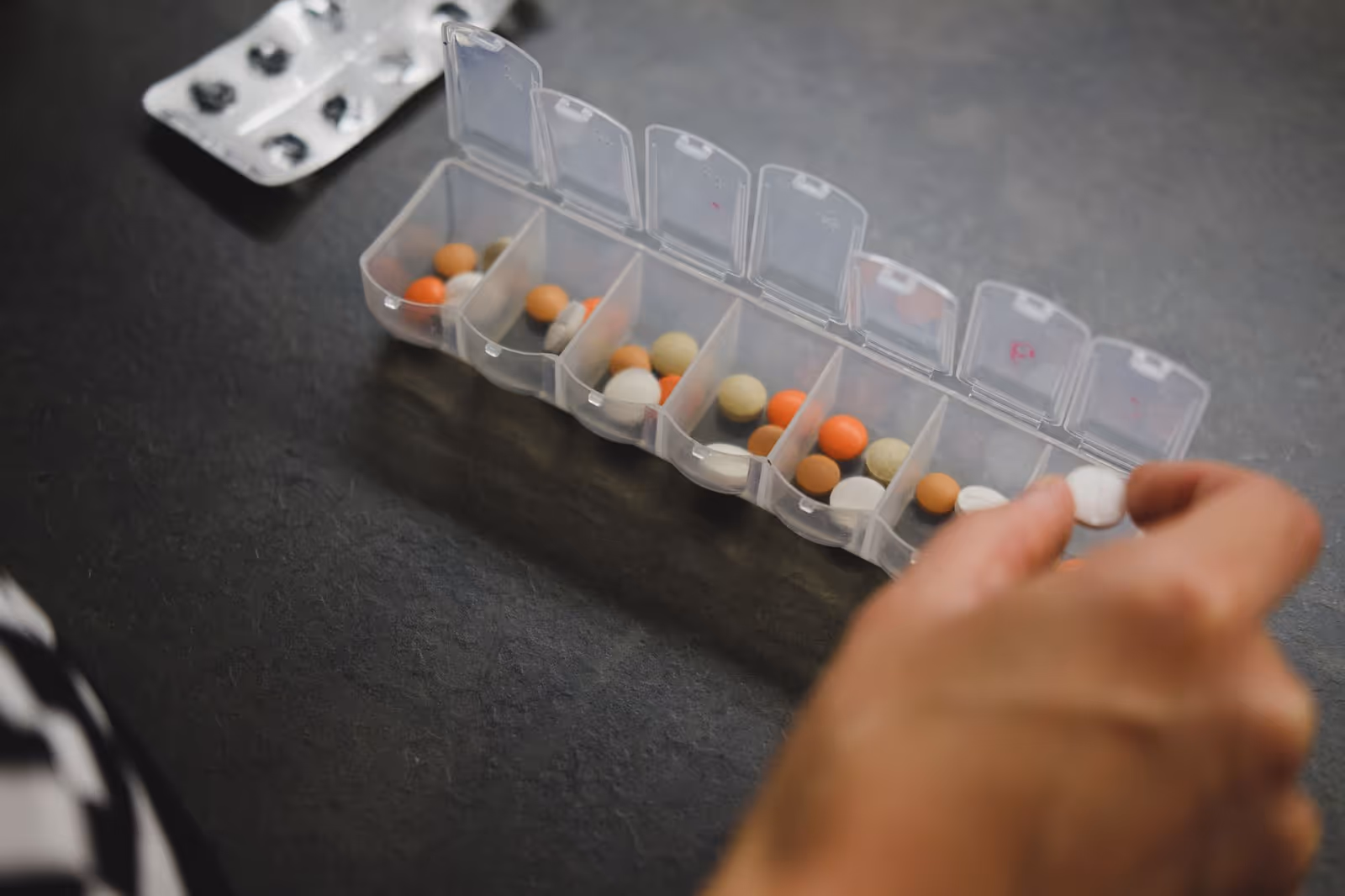 Open pill organizer filled with assorted tablets on a dark countertop.