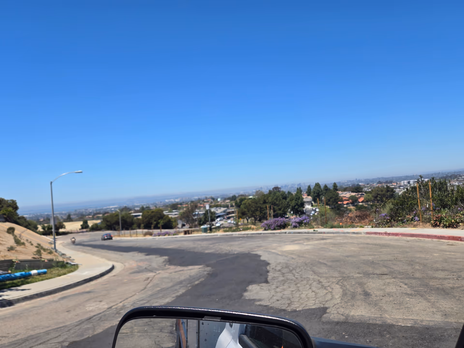 Hilly suburban road with curves, distant houses, and a clear blue sky.