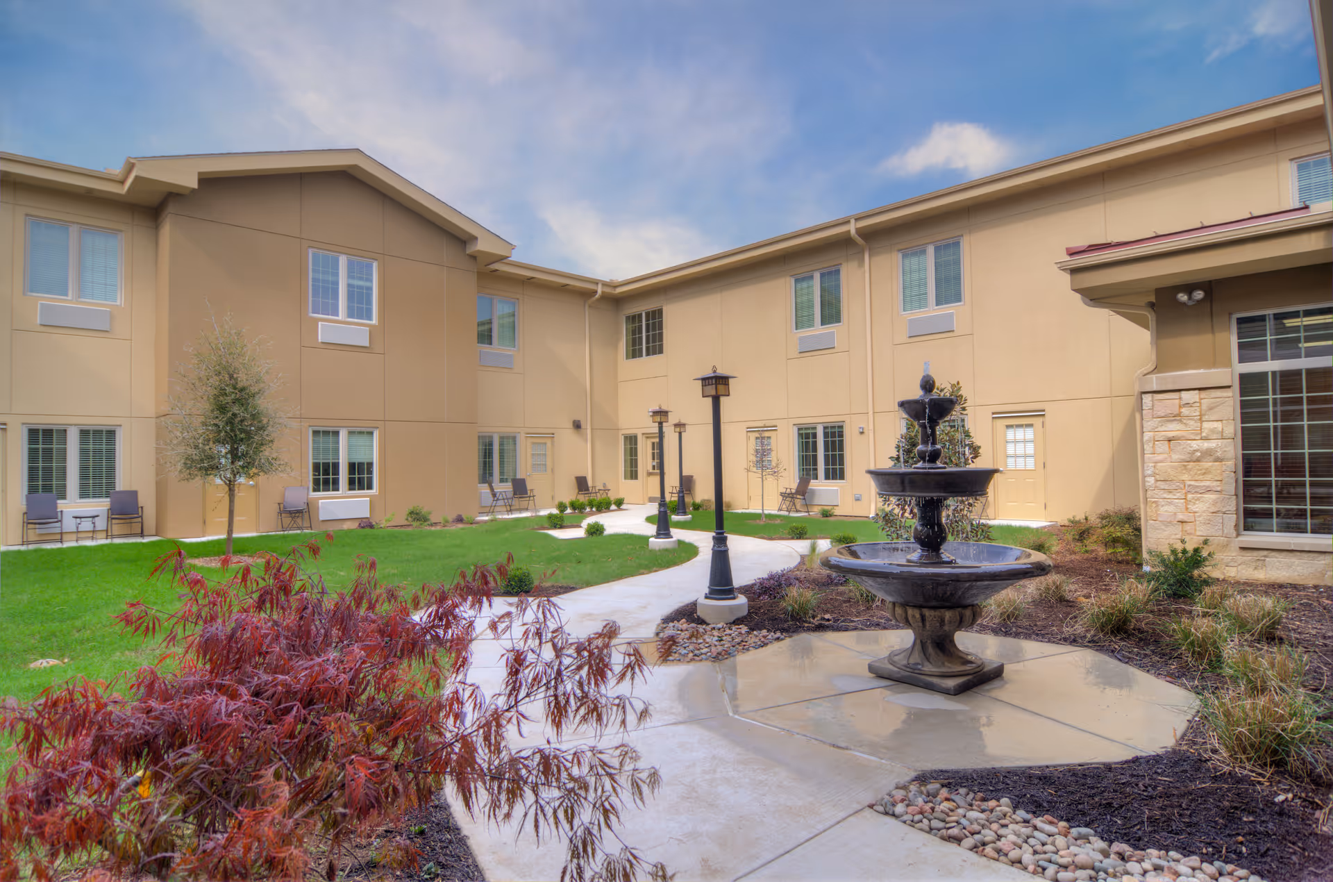 Sunny outdoor courtyard of a senior living facility with a fountain and benches