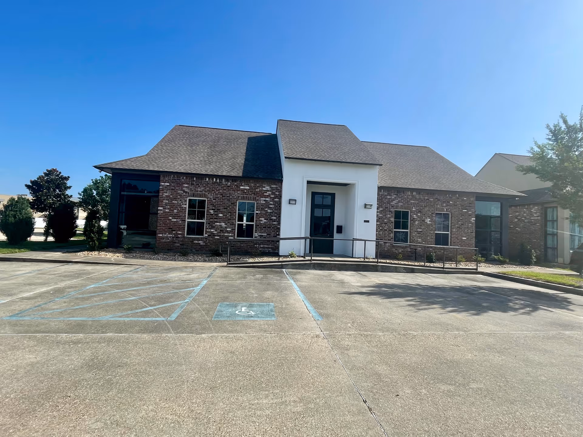 Brick senior care facility exterior with ramped entrance and parking in clear blue sky.