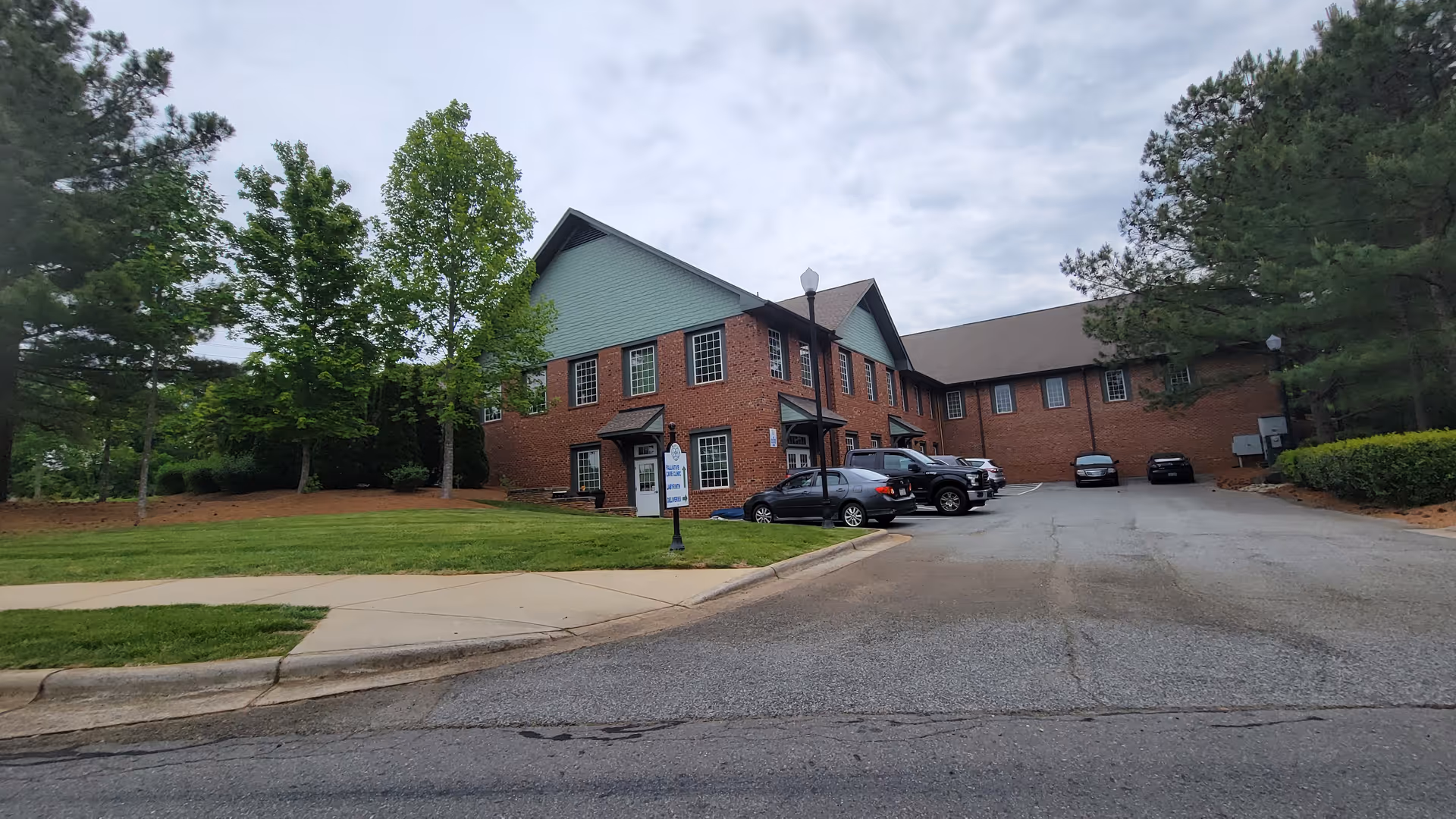 Brick senior living facility exterior with parked cars and trees.