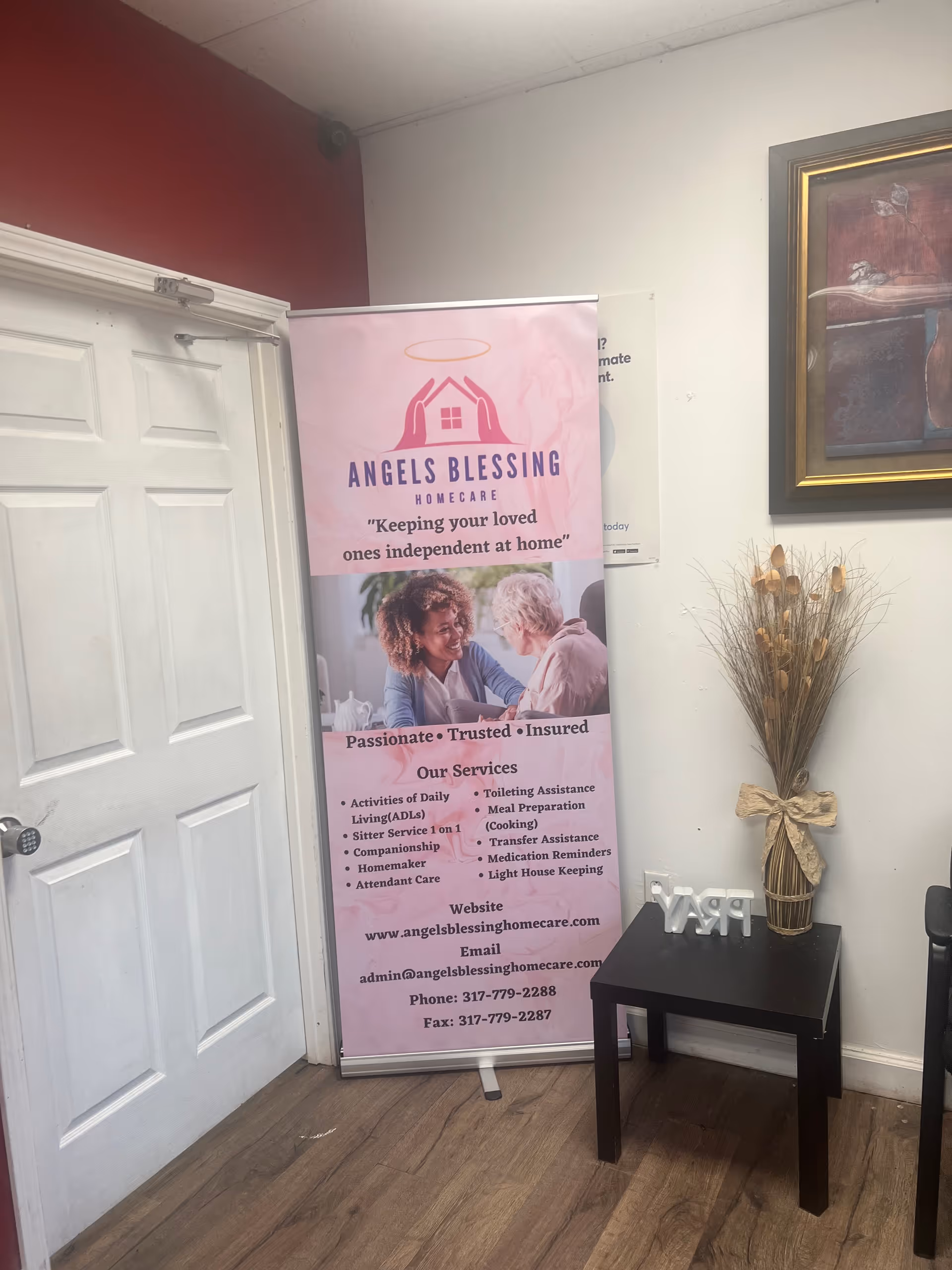 Indoor lobby corner with a pink Angels Blessing Homecare banner near a doorway.