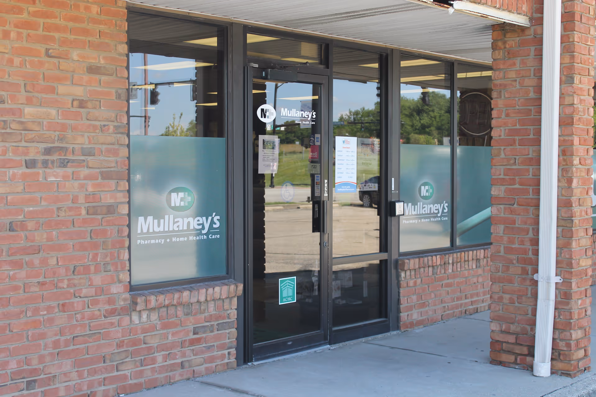Brick storefront with glass doors displaying Mullaney's Pharmacy and Home Health Care signage.