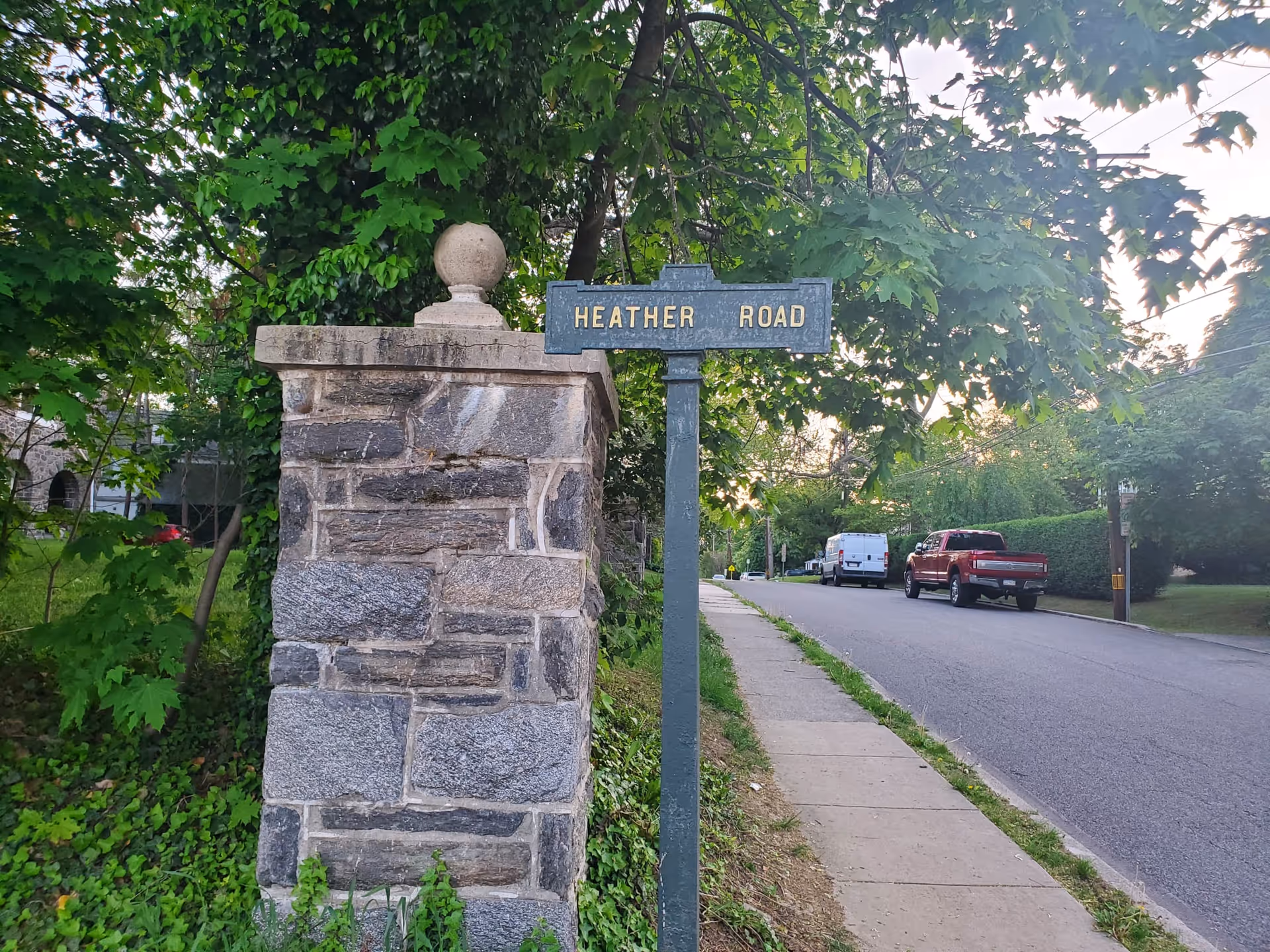 Stone pillar with Heather Road sign beside a sidewalk on a tree-lined residential street.