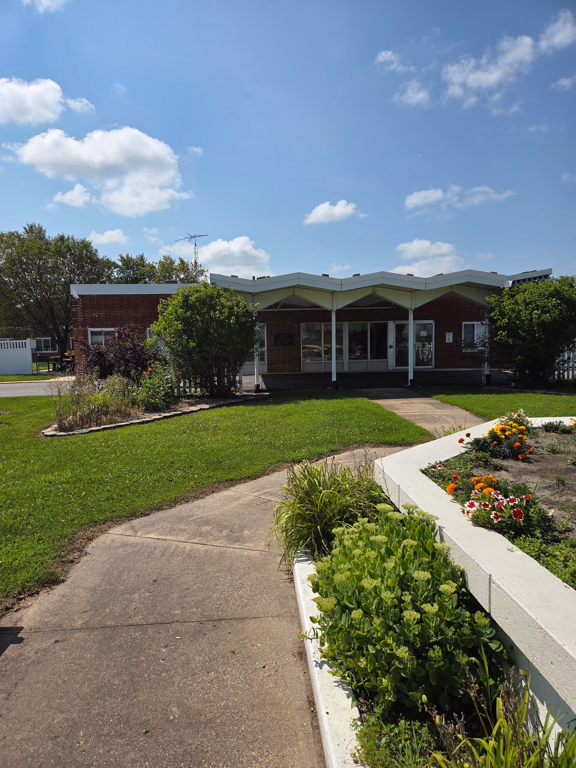 Elm Springs Assisted Living Apts front exterior shows a walkway and landscaped garden beds.