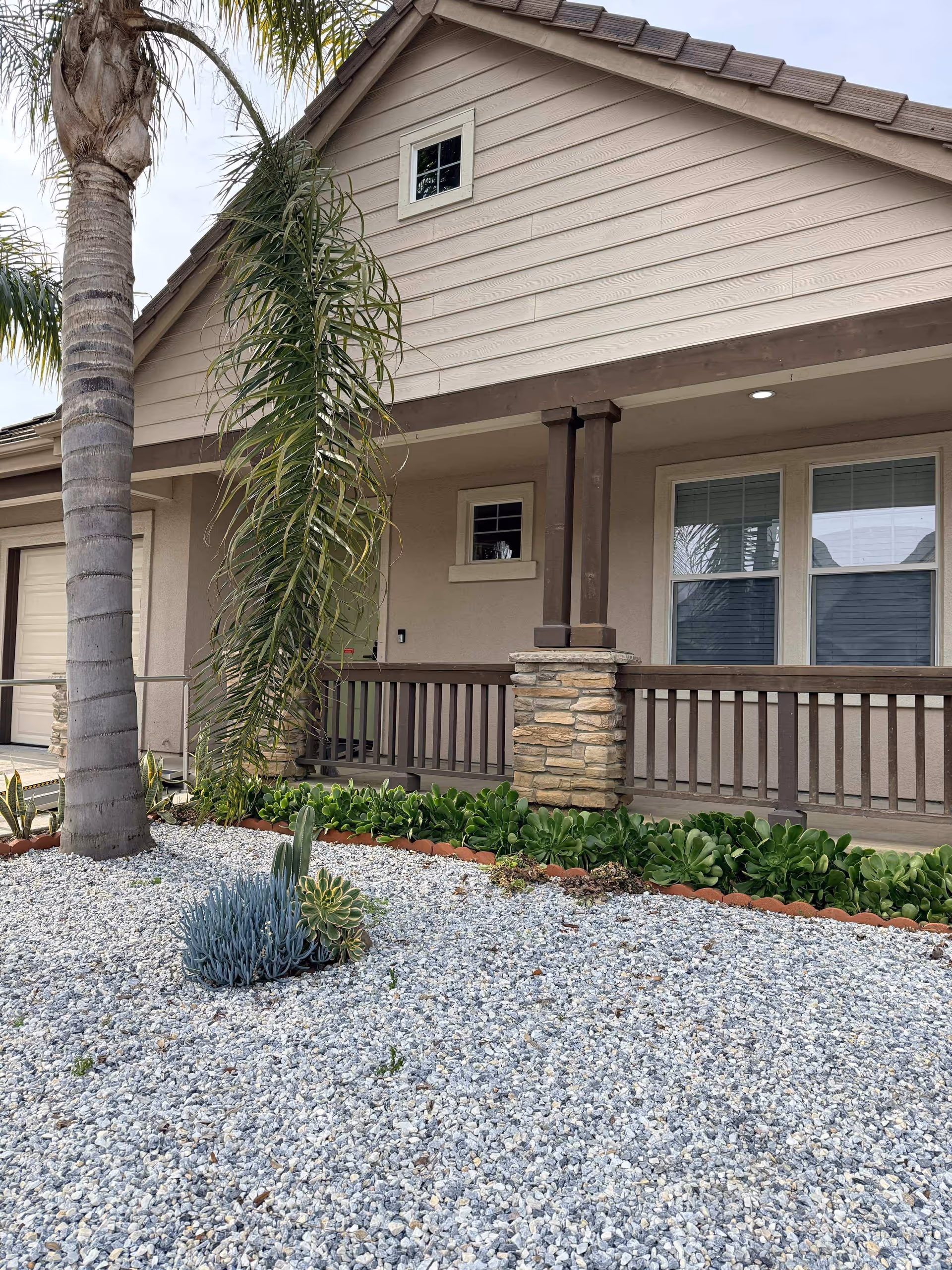 Front exterior of a beige senior living facility with a covered porch and drought landscaping.