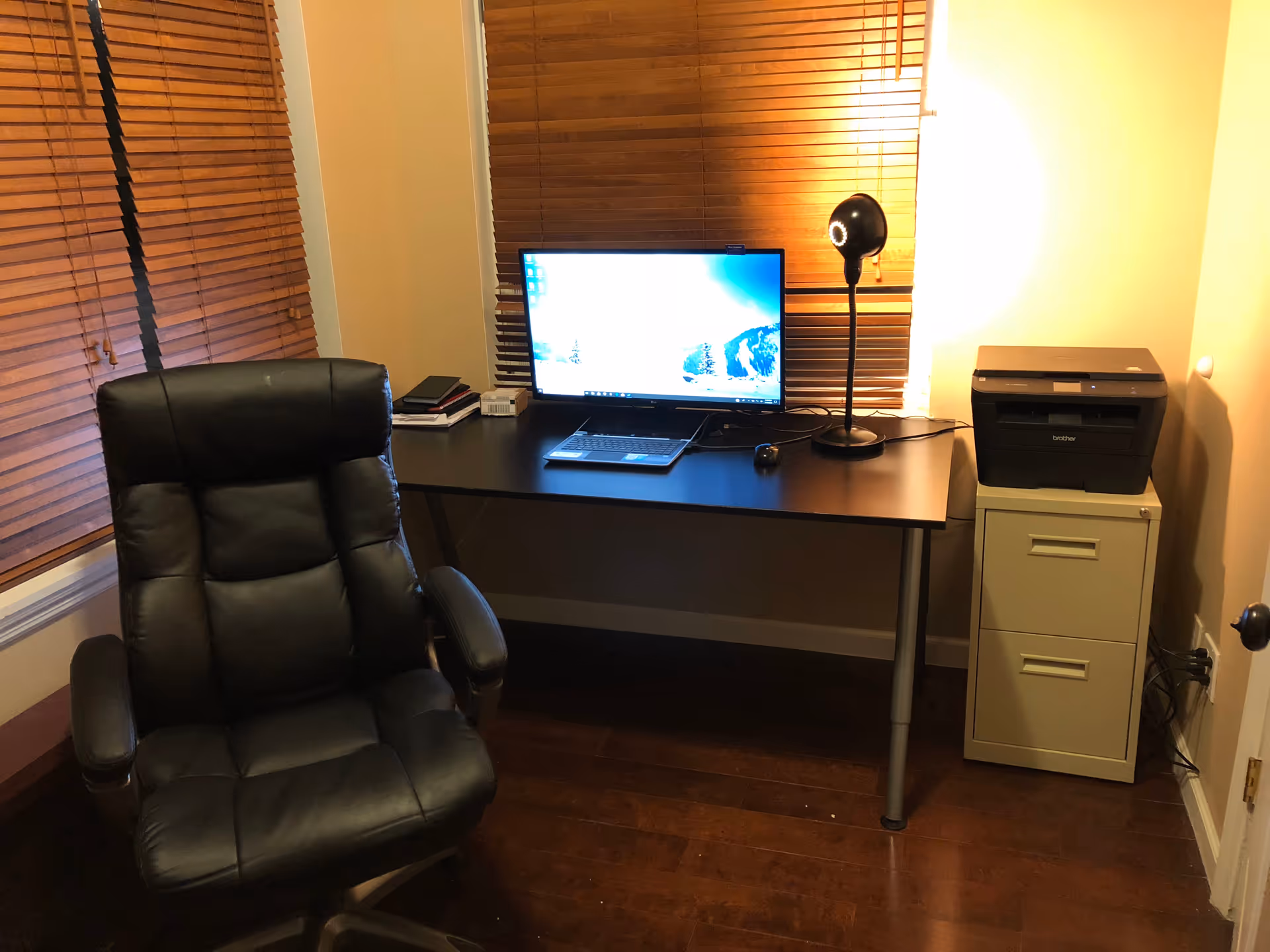 Home office setup with desk, computer monitor, laptop, printer, and a black leather chair.