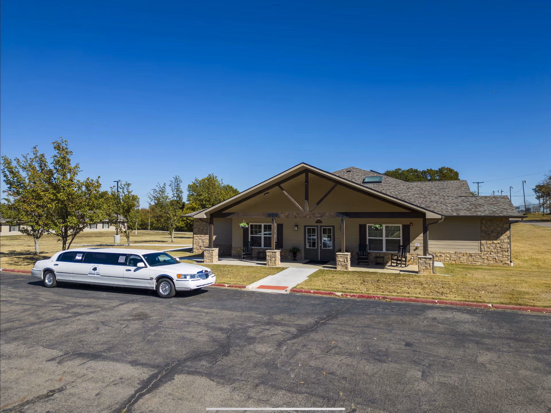 A single-story beige senior living facility with stone accents, a covered entrance, and a white limousine.