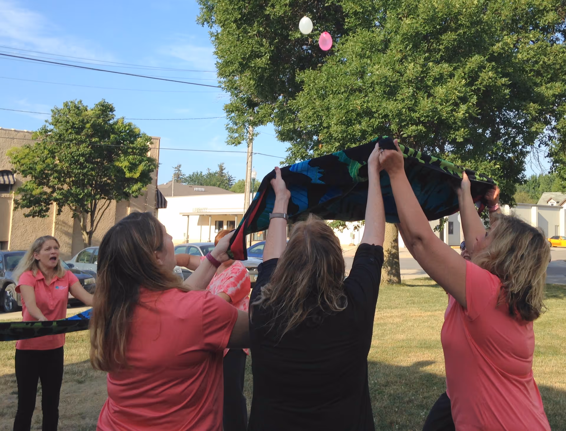 Group of people outdoors holding up a colorful fabric together.