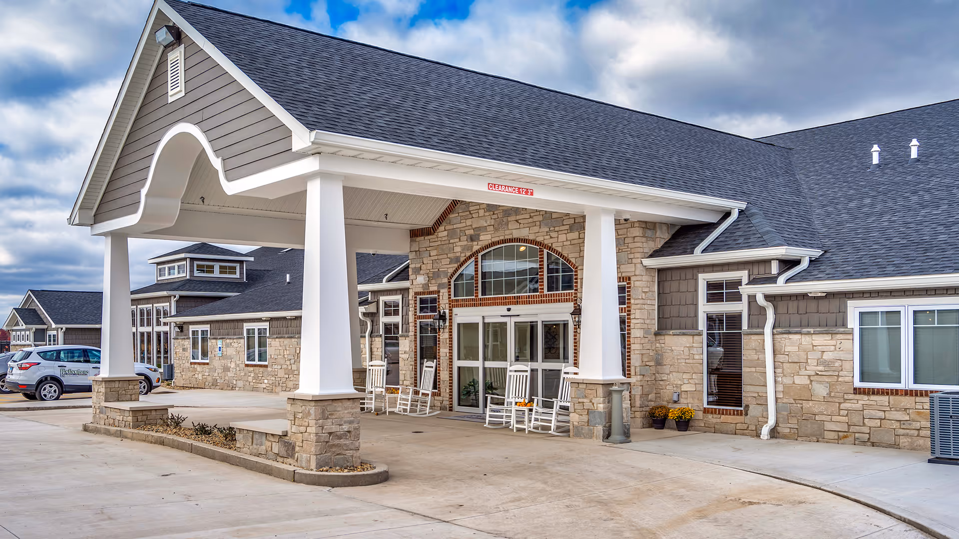 Exterior view of Reflections Memory Care facility with stone facade and rocking chairs at entrance