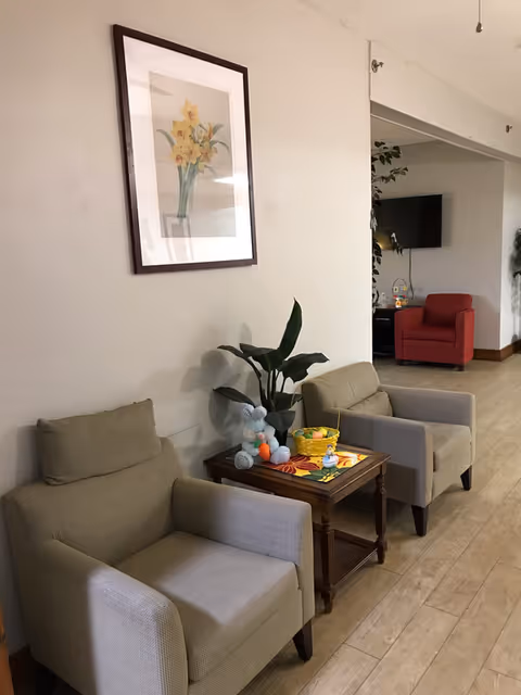 Cozy Hillside Assisted Living lounge with beige armchairs, a small table, plant, and wall art.