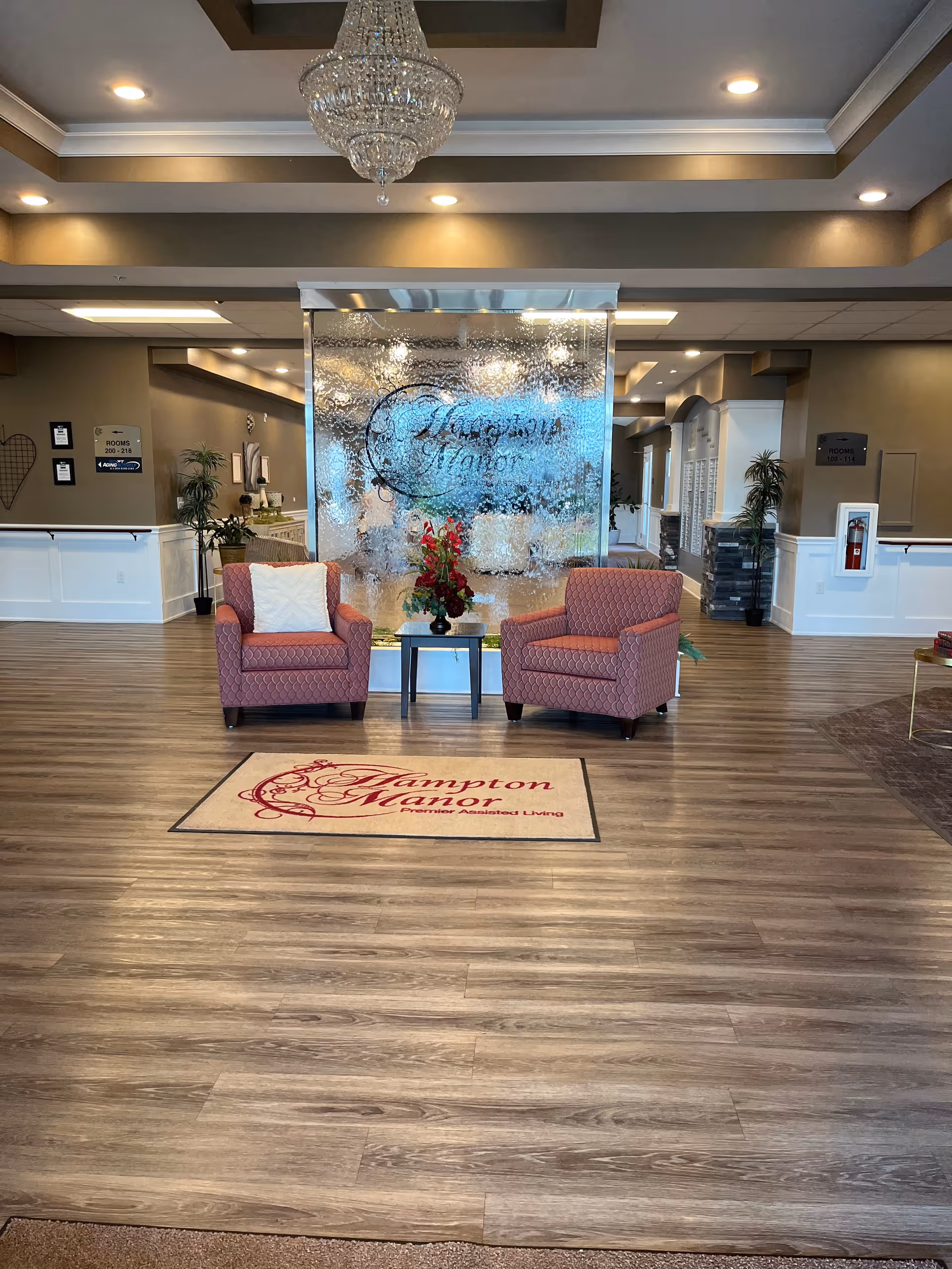 Elegant hotel-style lobby with chandelier, two pink armchairs, glass divider, Hampton Manor rug.