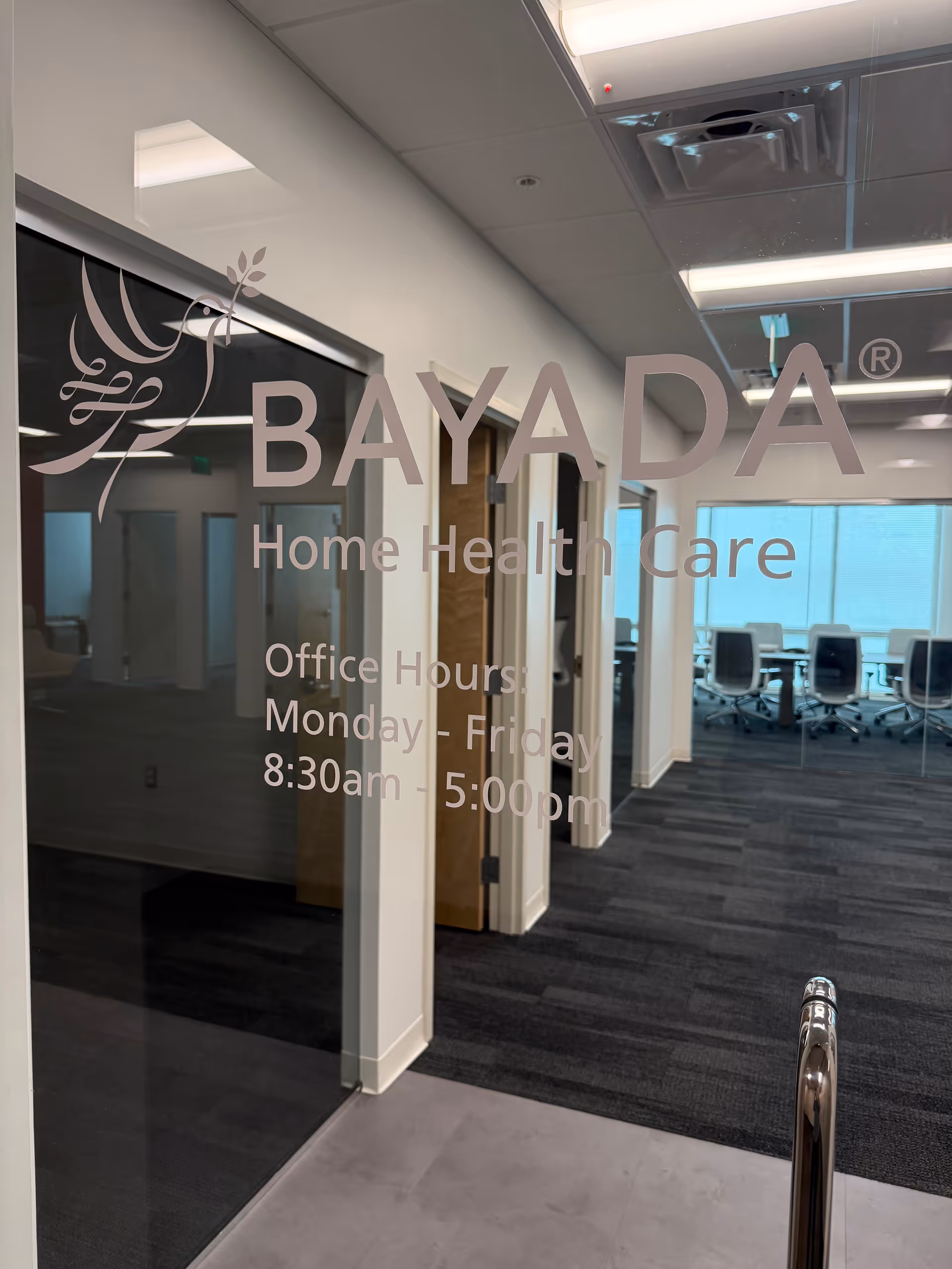 Glass door displays BAYADA Home Health Care branding; office conference room visible beyond.