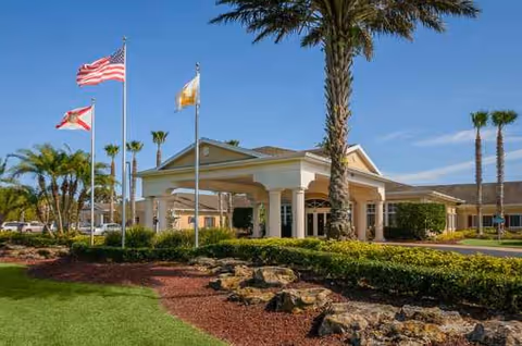 Entrance of Life Care Center of Palm Bay with flags, palm trees, and landscaped driveway.