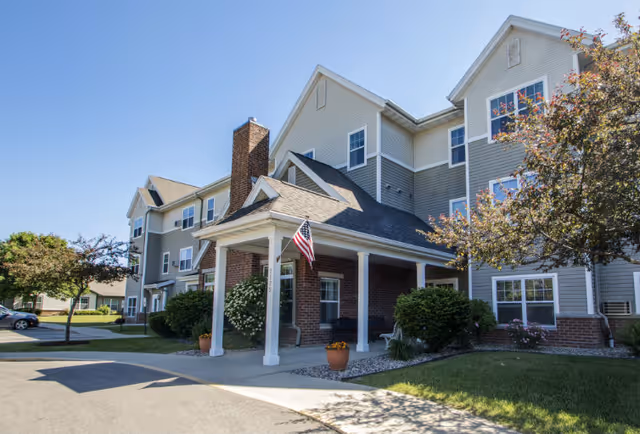 Senior living facility exterior with a covered entrance, brick columns, and flag.