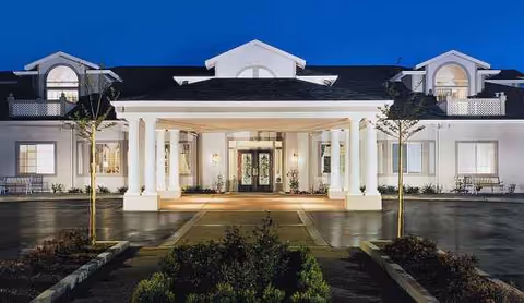 Nighttime view of Ivy Park at San Ramon's illuminated front entrance with tall white columns.