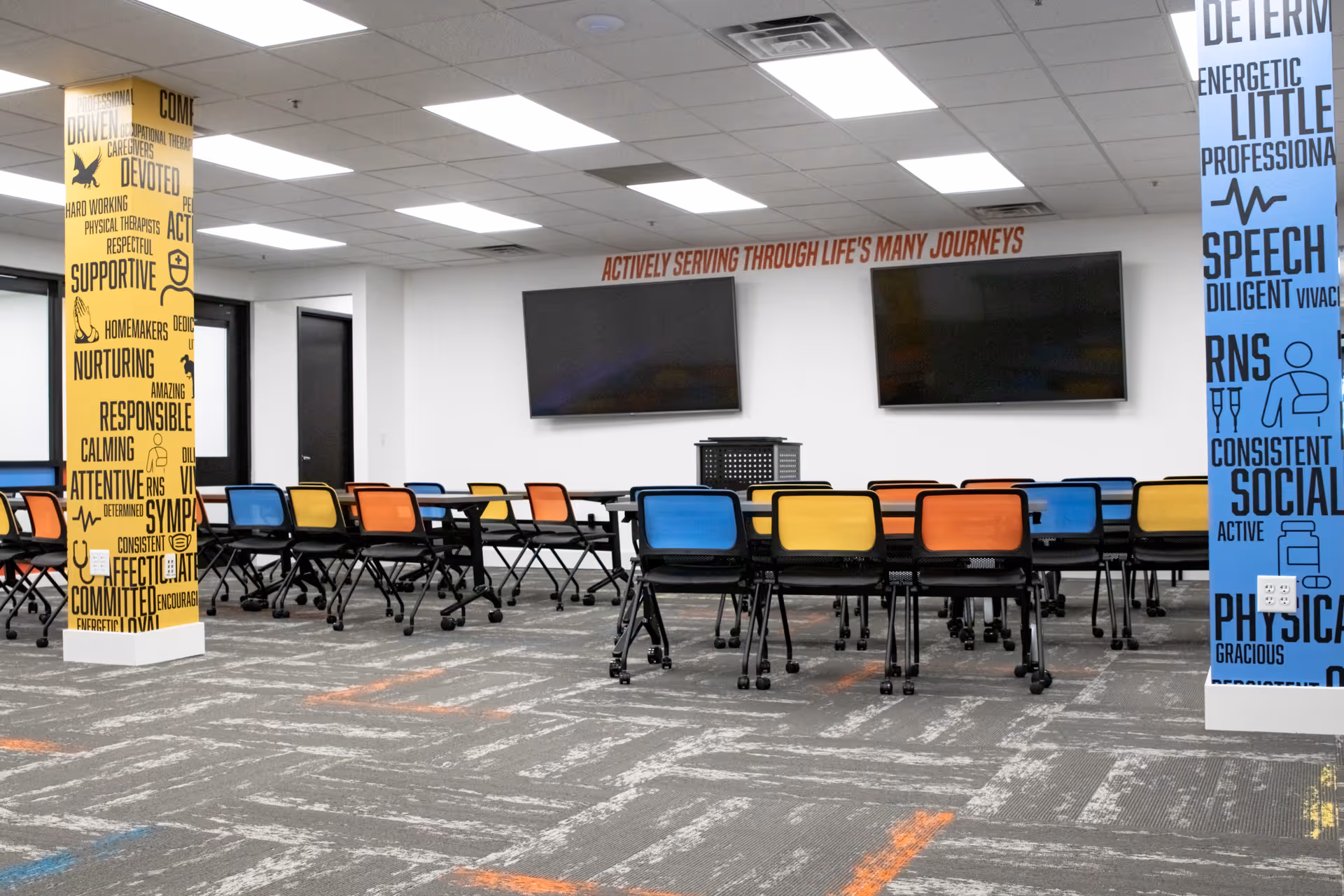 Colorful chairs surround long tables in a bright, modern community room at a care facility.