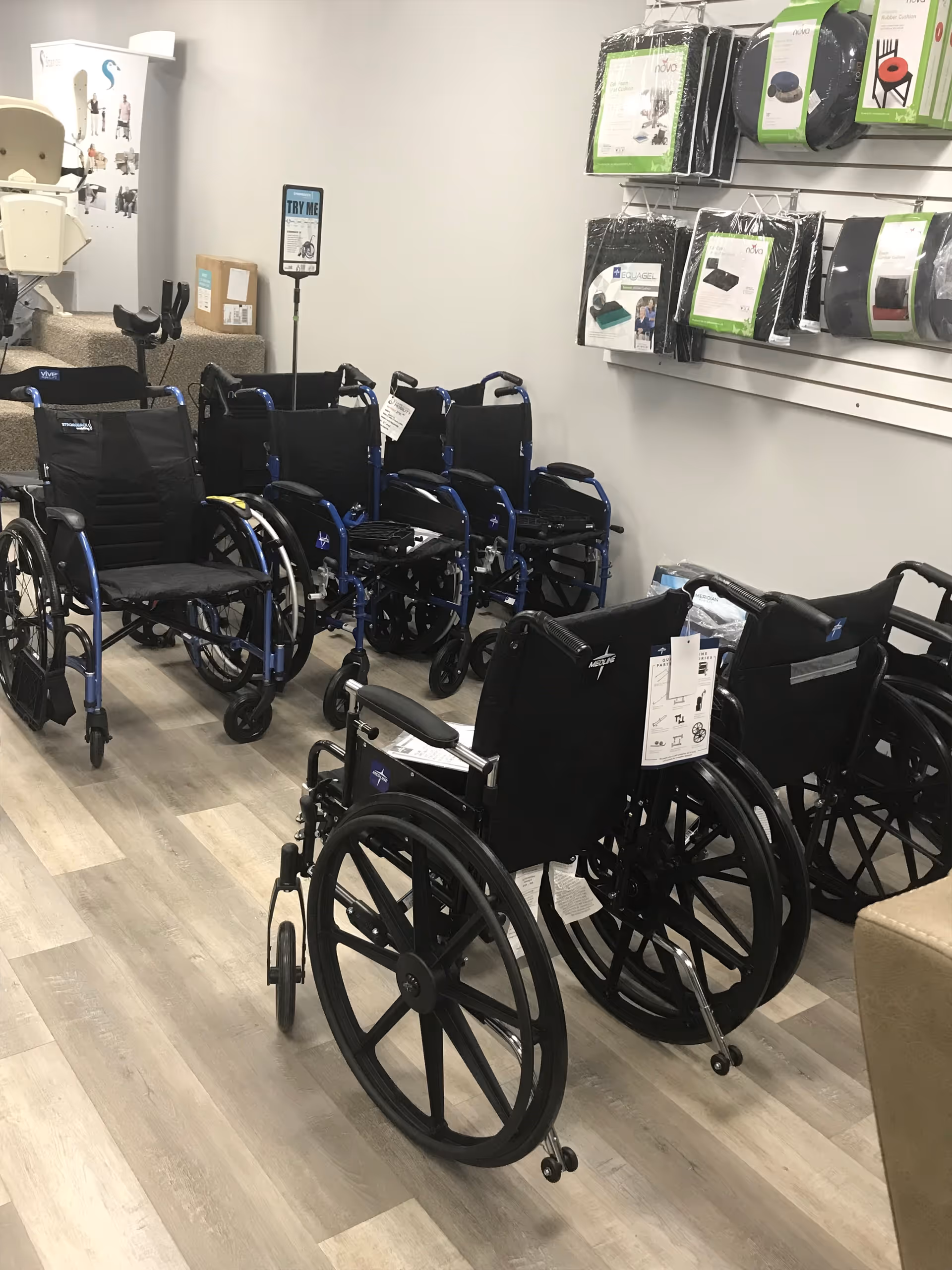 Indoors, multiple wheelchairs lined up on a wood floor in a mobility equipment showroom.