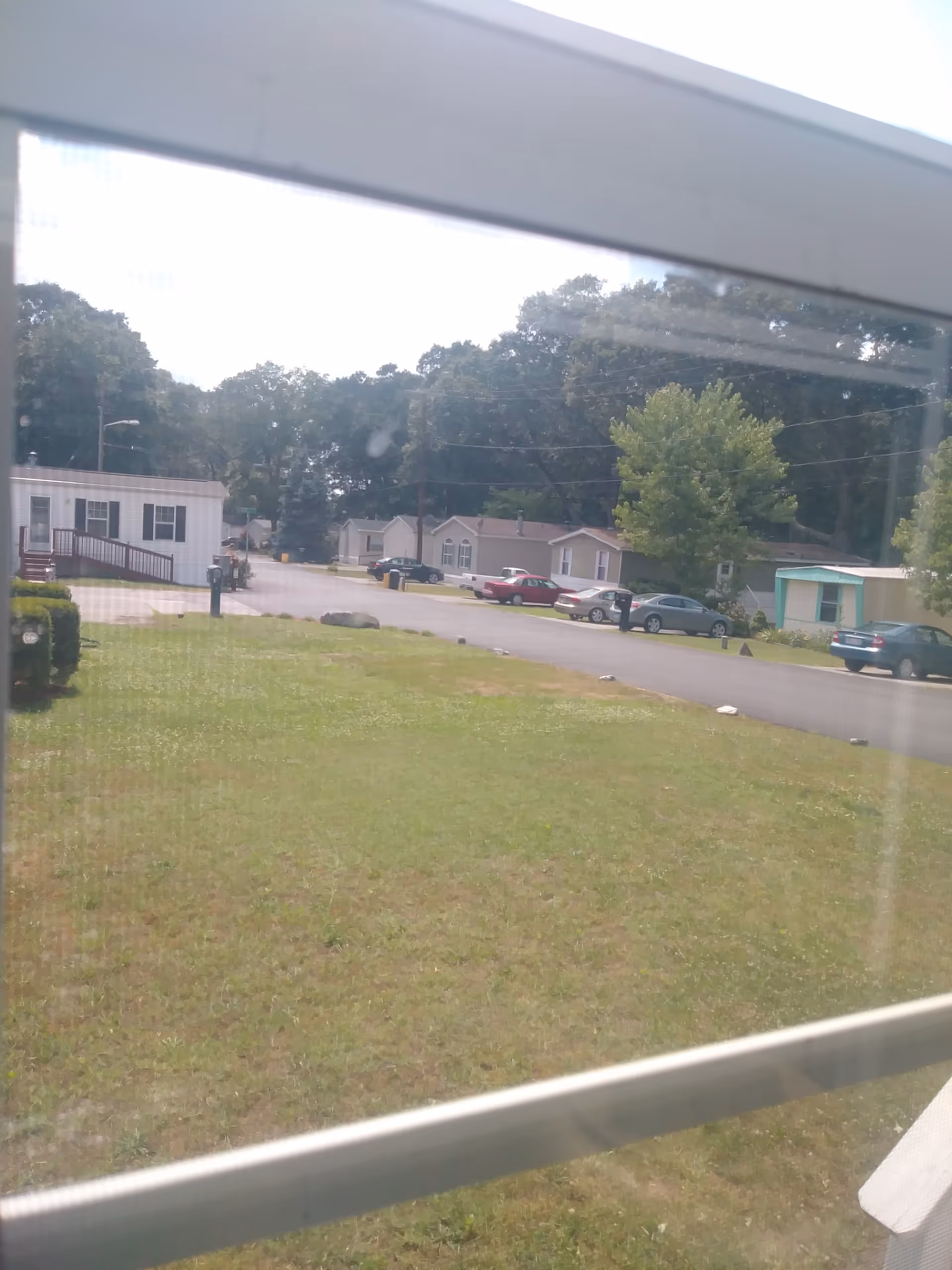 View of a mobile home park with grassy foreground, trailers, and parked cars.
