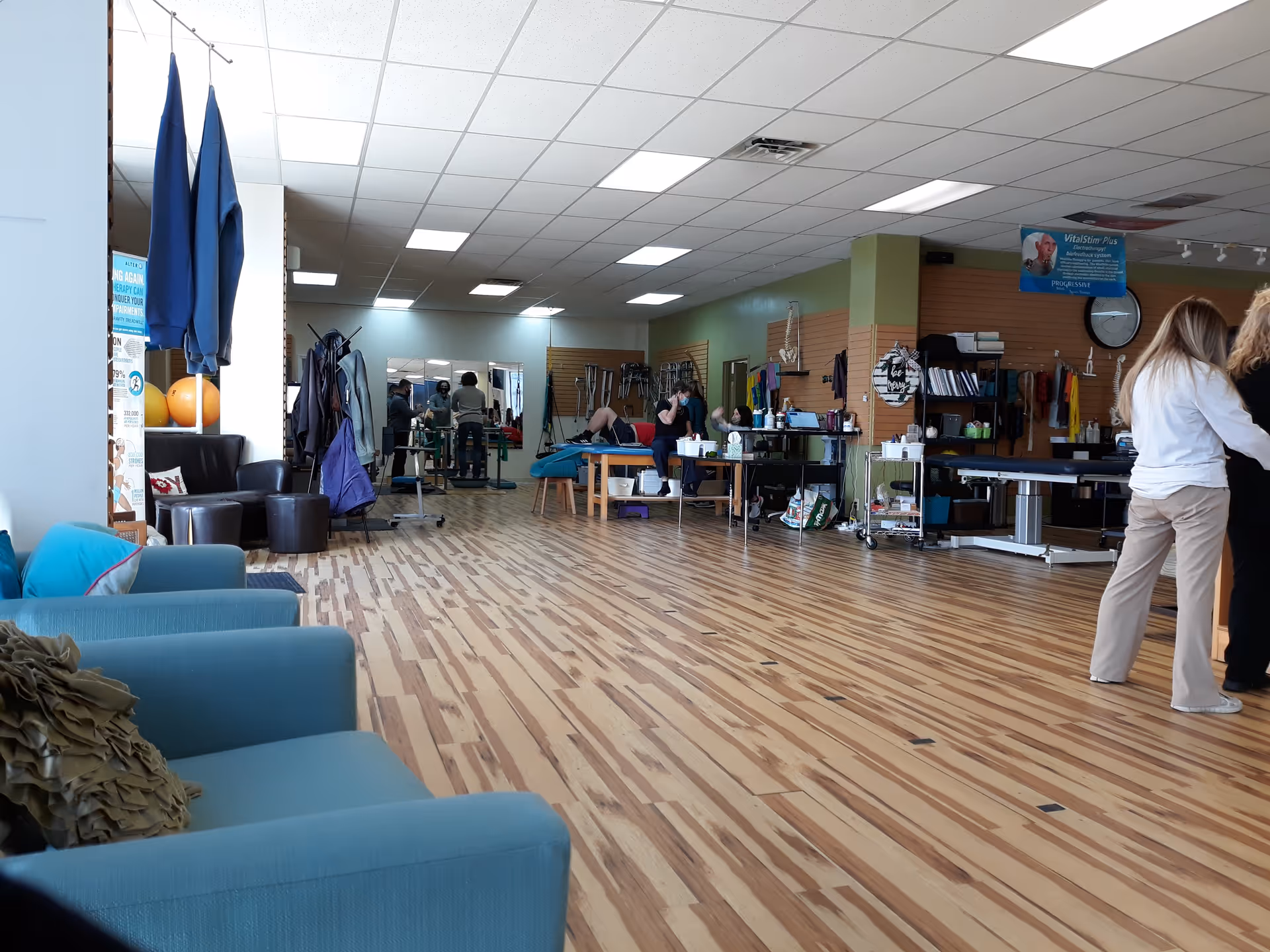 Open rehabilitation room with therapy tables, equipment, and staff assisting clients.