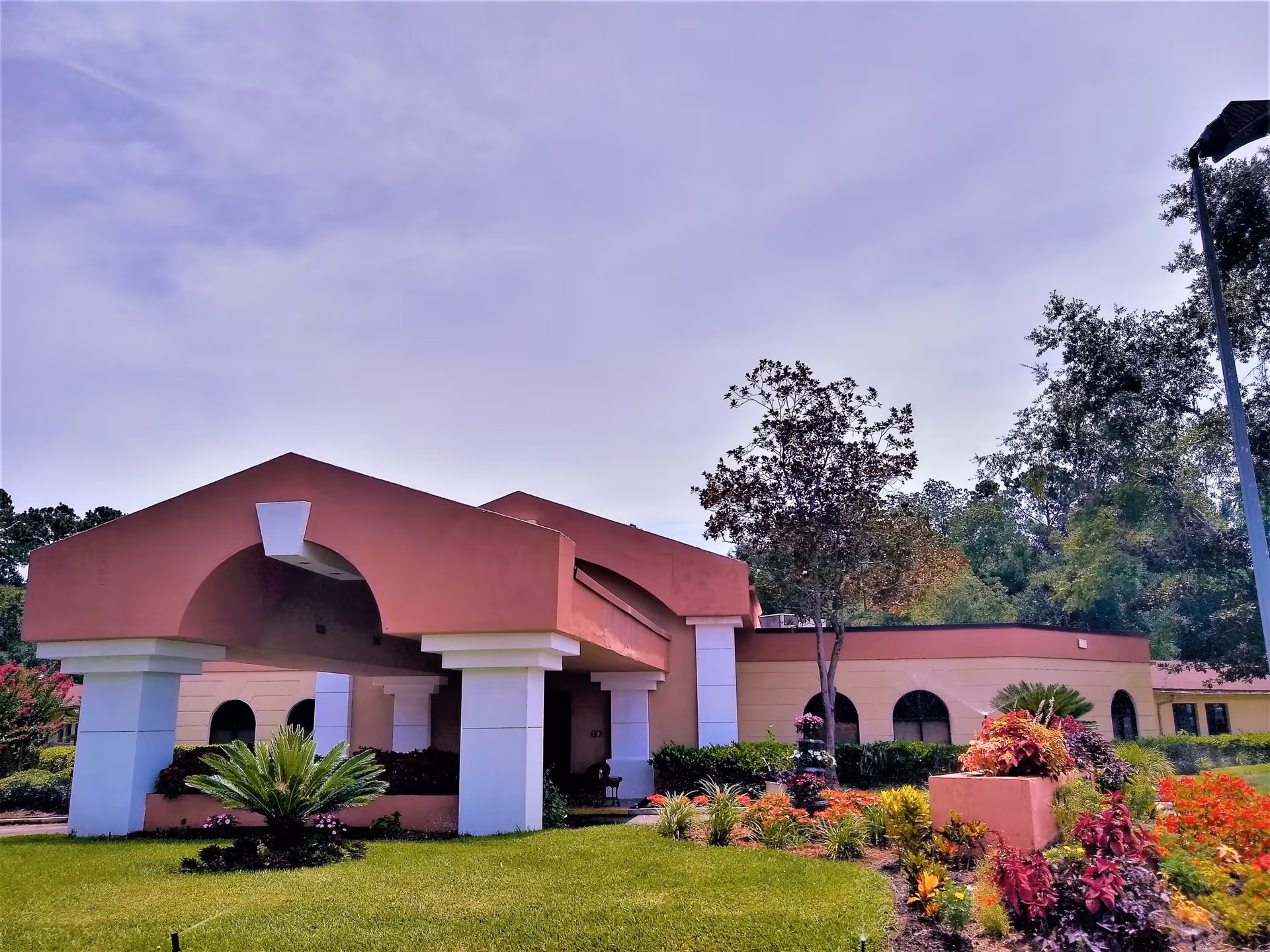 Pink stucco assisted living building with arches, pillars, and landscaped garden in front.