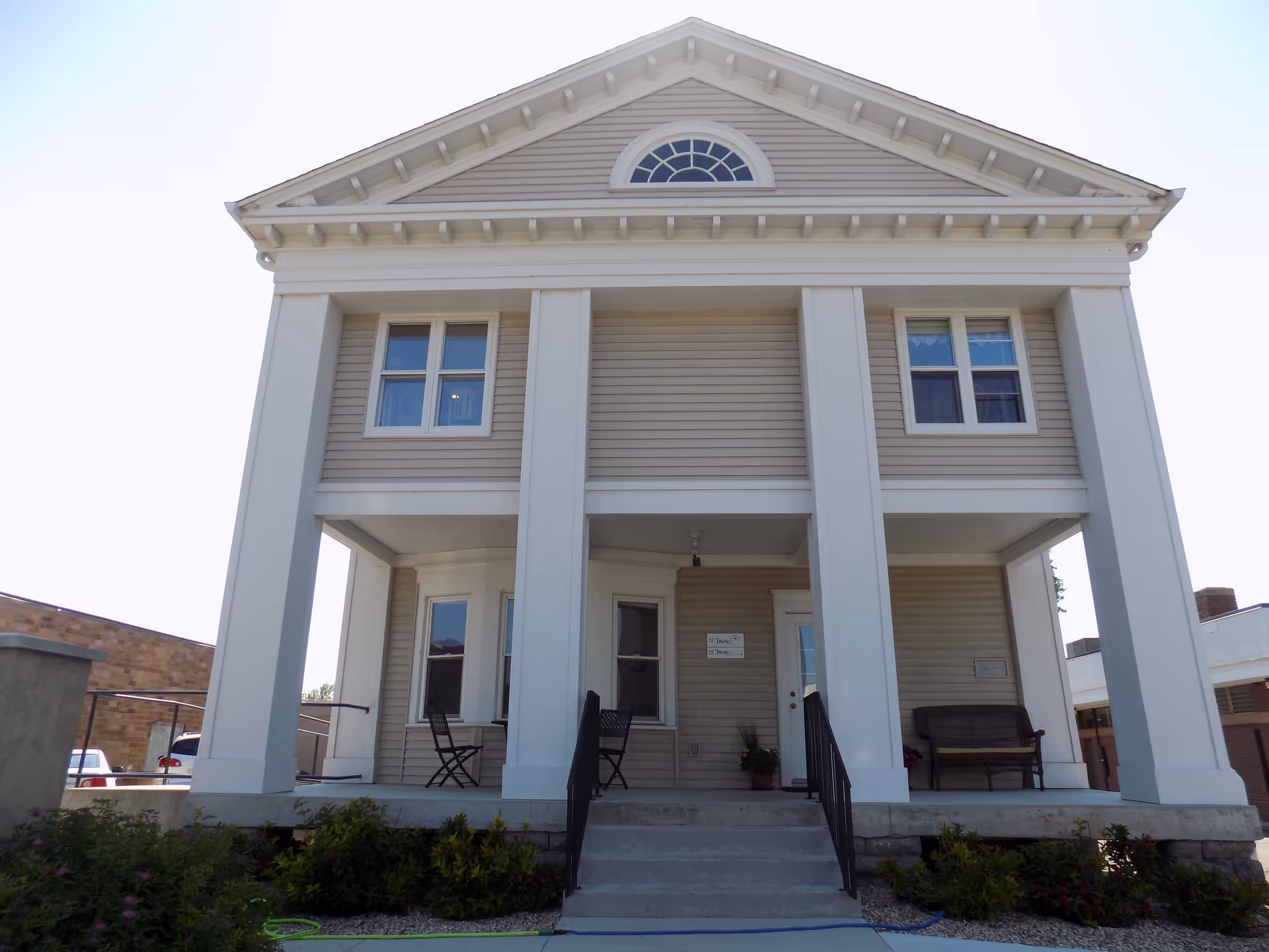 Two-story beige building with tall white columns and a small porch.
