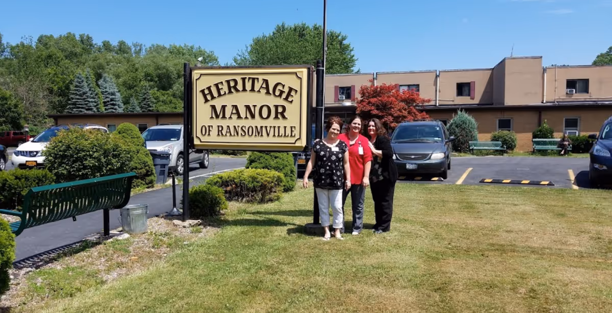 Four people pose near Heritage Manor of Ransomville sign outside the building.