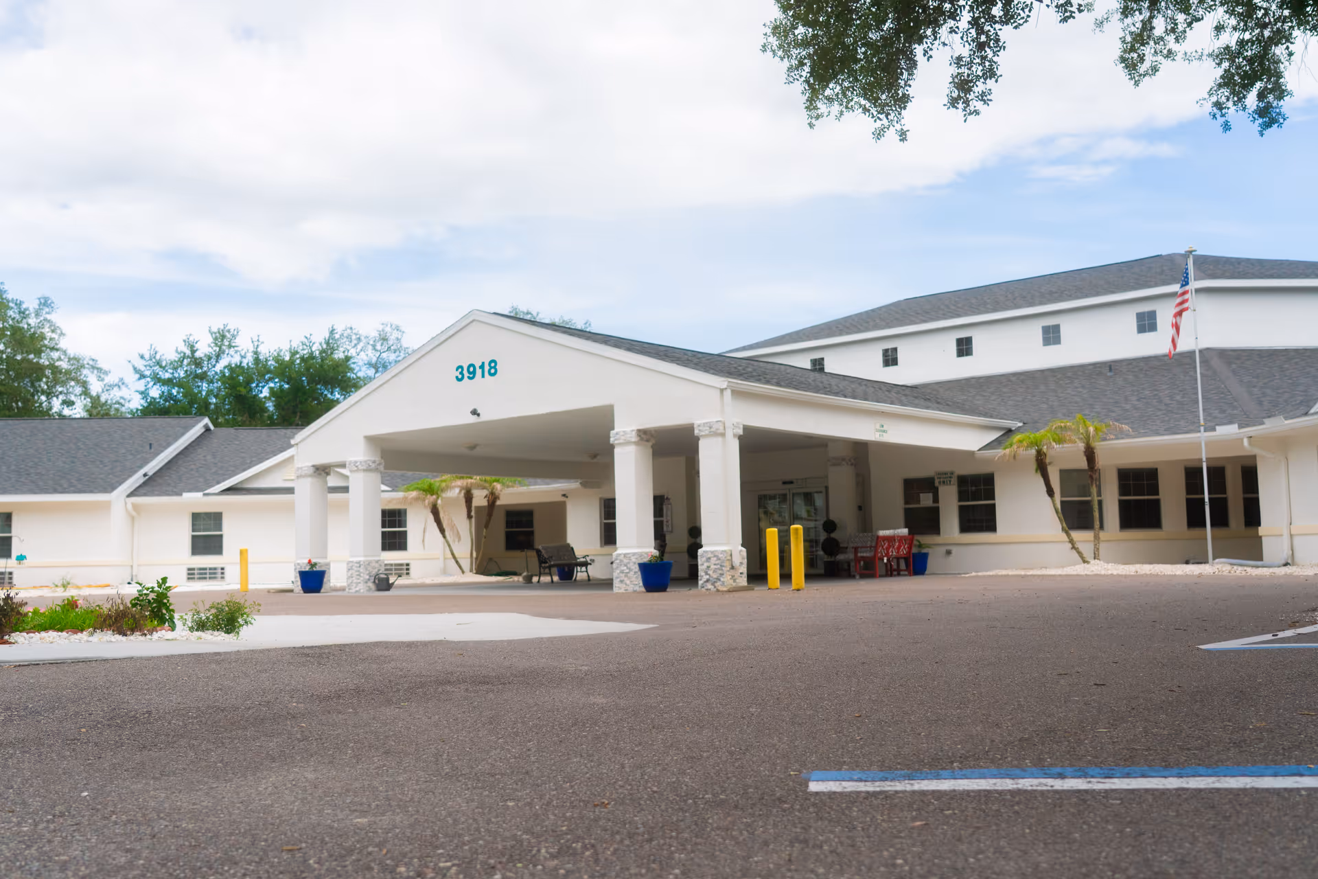 White senior living facility with a covered entrance, columns, palm trees, and a spacious parking lot.