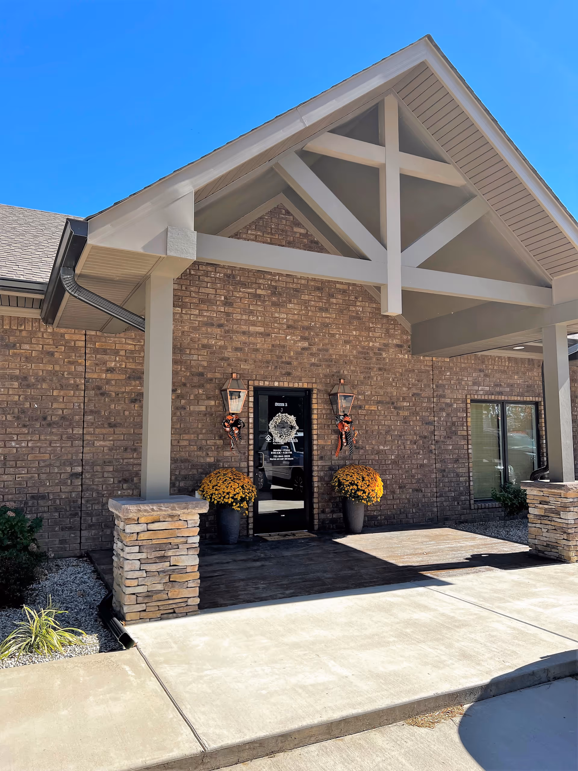Front entrance of brick senior living facility with a covered porch, planters, and wreaths.