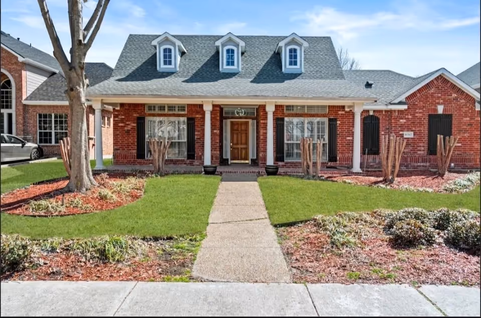 Brick senior living facility exterior with a covered front porch and manicured lawn.