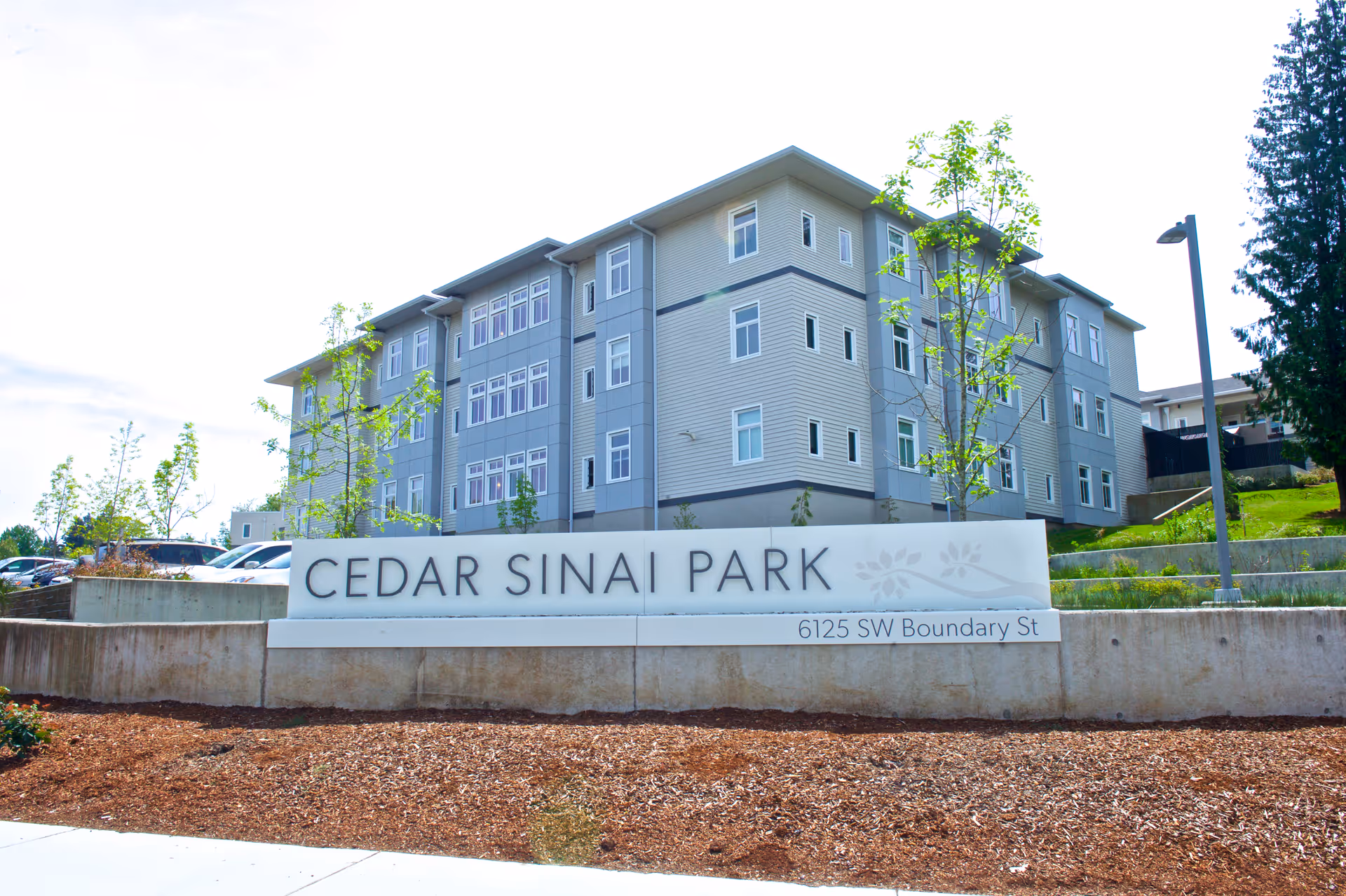 Exterior of a modern multi-story senior living building with a Cedar Sinai Park sign.