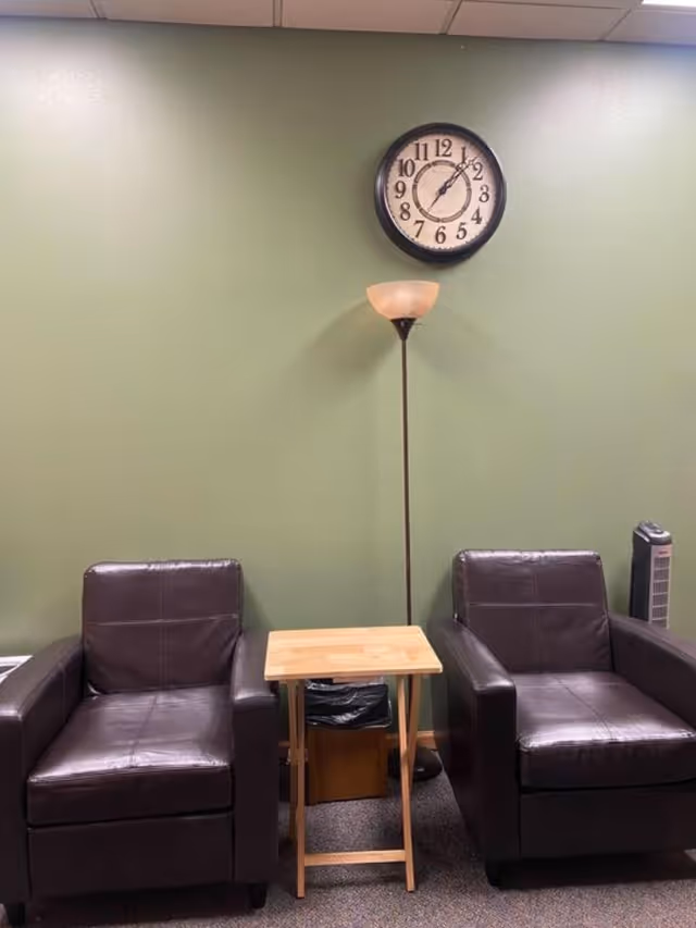 Two dark leather chairs flank a small wooden table against a green wall.