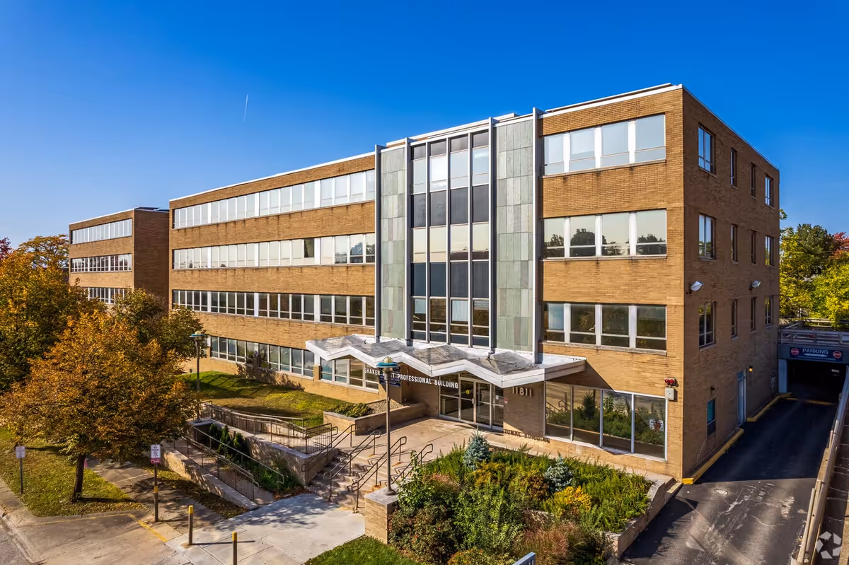 Exterior view of a brick multi-story facility with a glass entry and landscaped surroundings.
