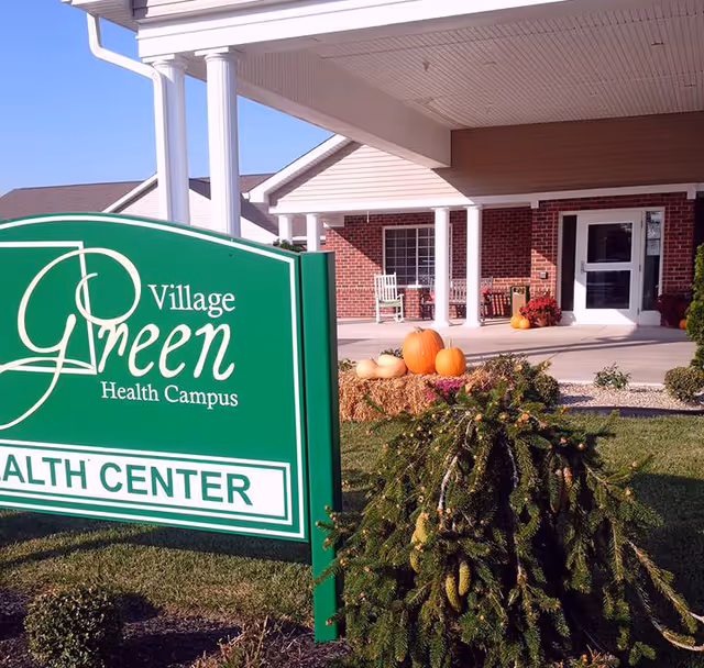Village Green Health Campus sign sits beside the building entrance with pumpkins outside.