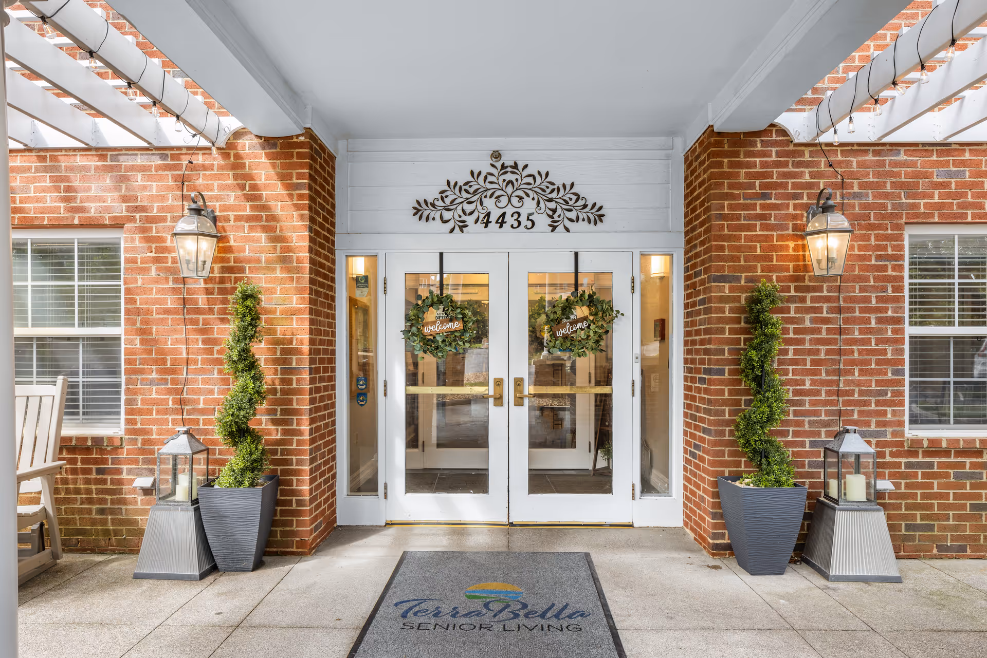 Brick exterior entrance with glass doors, wreaths, and tall planters at TerraBella Senior Living.