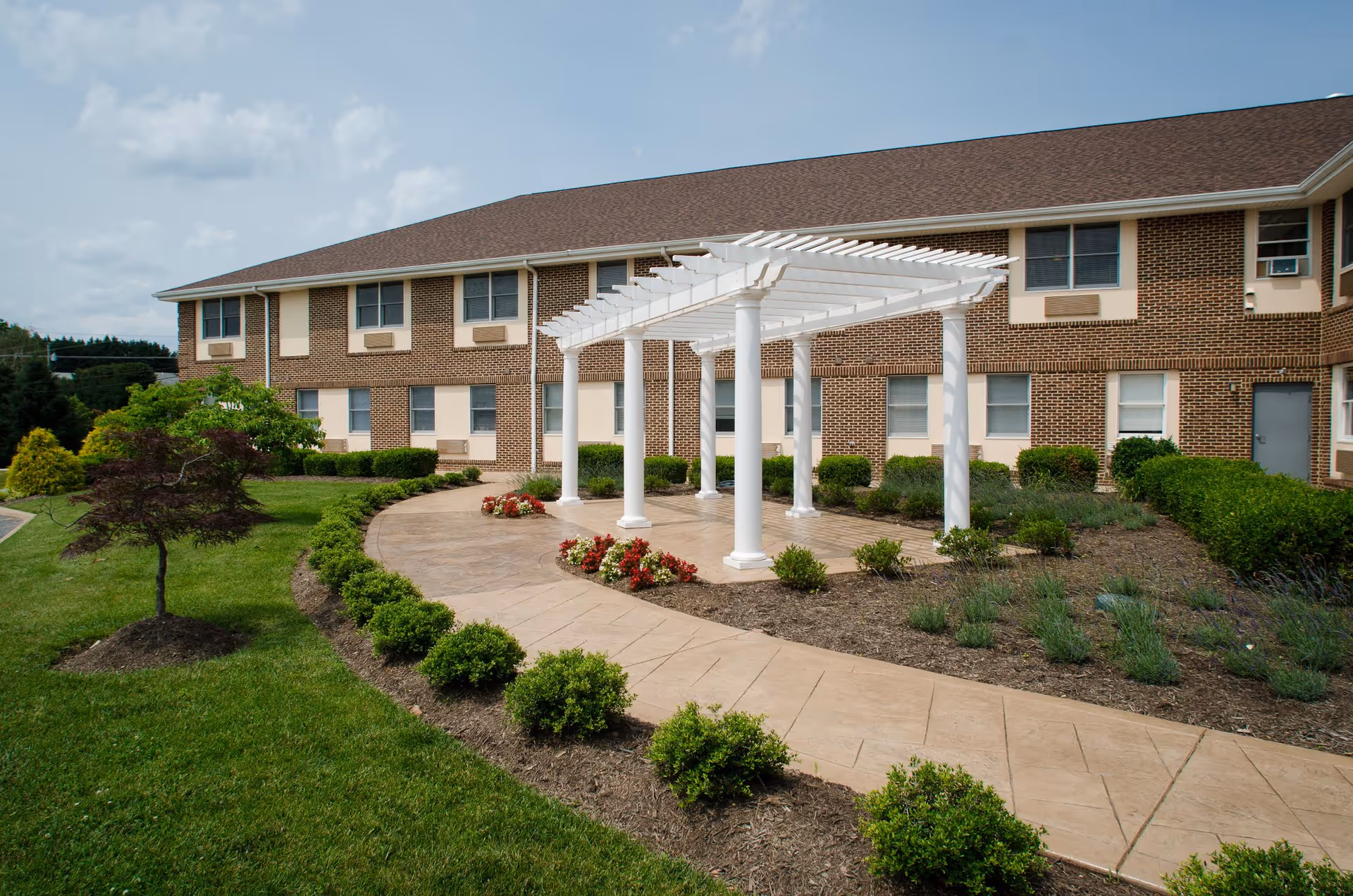 Front exterior view of Commonwealth Senior Living at Front Royal with white pergola and landscaped walkway.