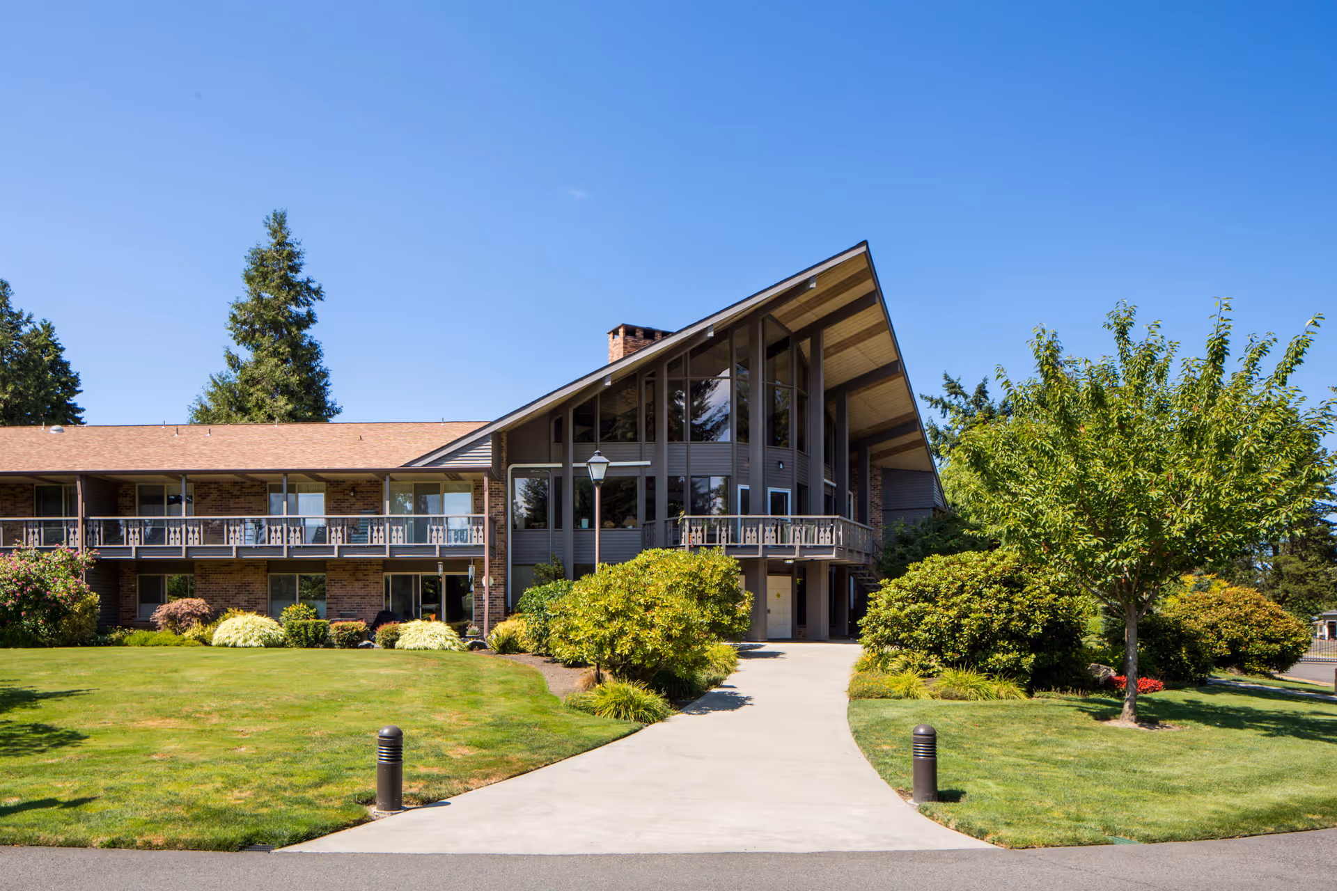 Two-story building with a prominent A-frame entrance, balconies and a manicured lawn under a clear blue sky.