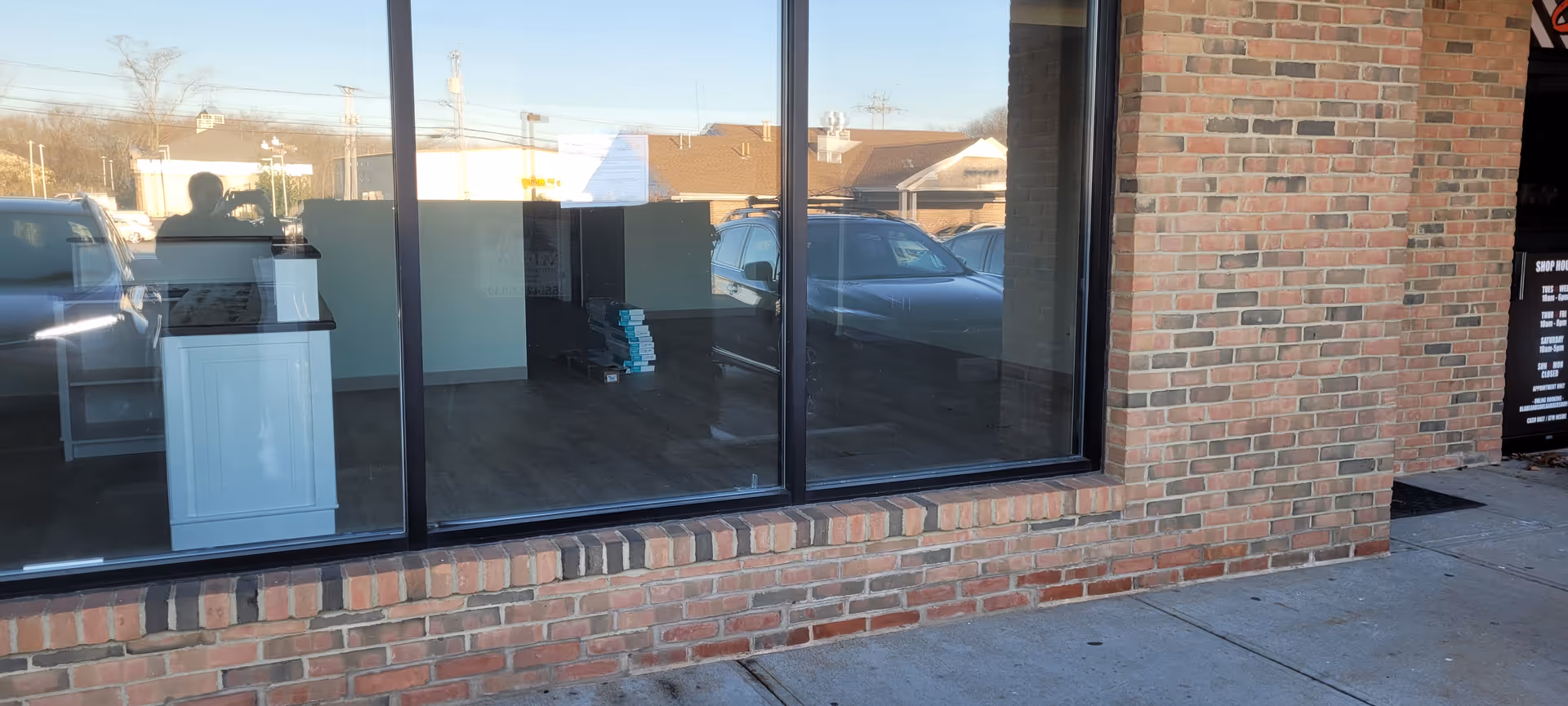 Brick storefront with large windows showing a reception area inside and parked cars outside.