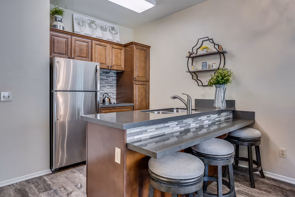Modern kitchen with stainless refrigerator, wooden cabinets, island sink, and three gray stools.