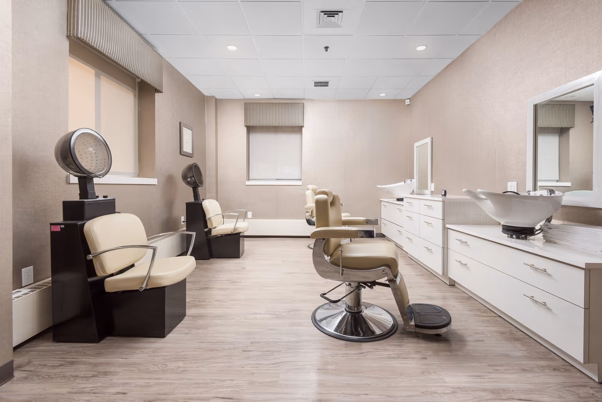 Well-lit salon room with styling chairs, hooded hair dryers, wash basins and mirrors.
