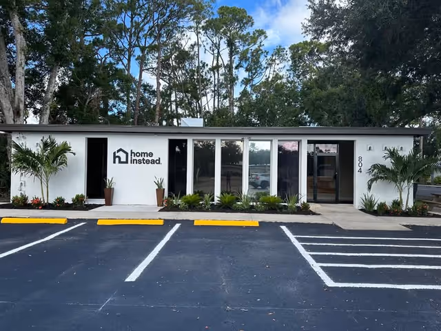 A single-story building with Home Instead signage, glass windows, landscaped front, and parking lot.