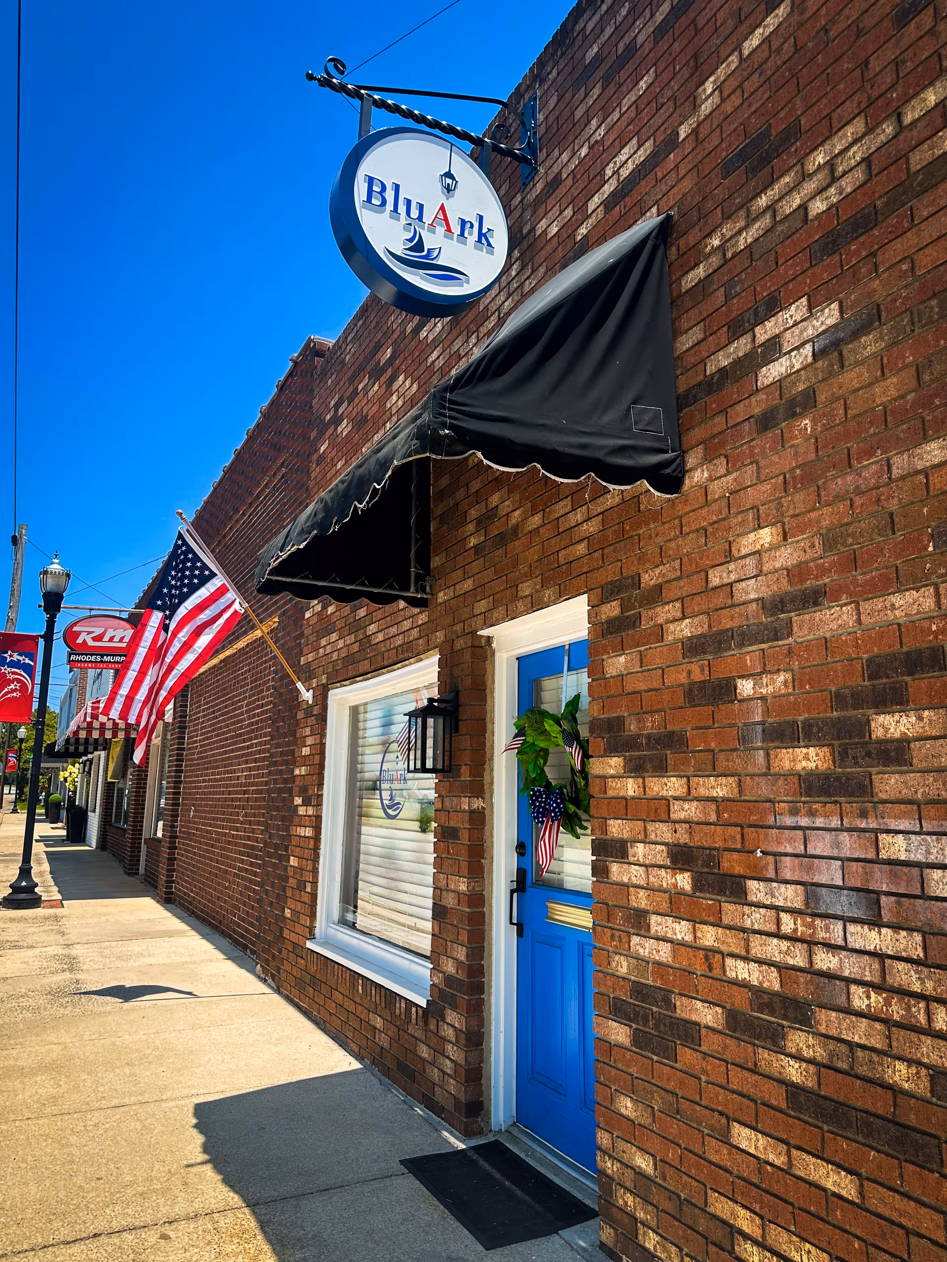 Exterior brick building with BluArk sign, blue door, and waving American flag.